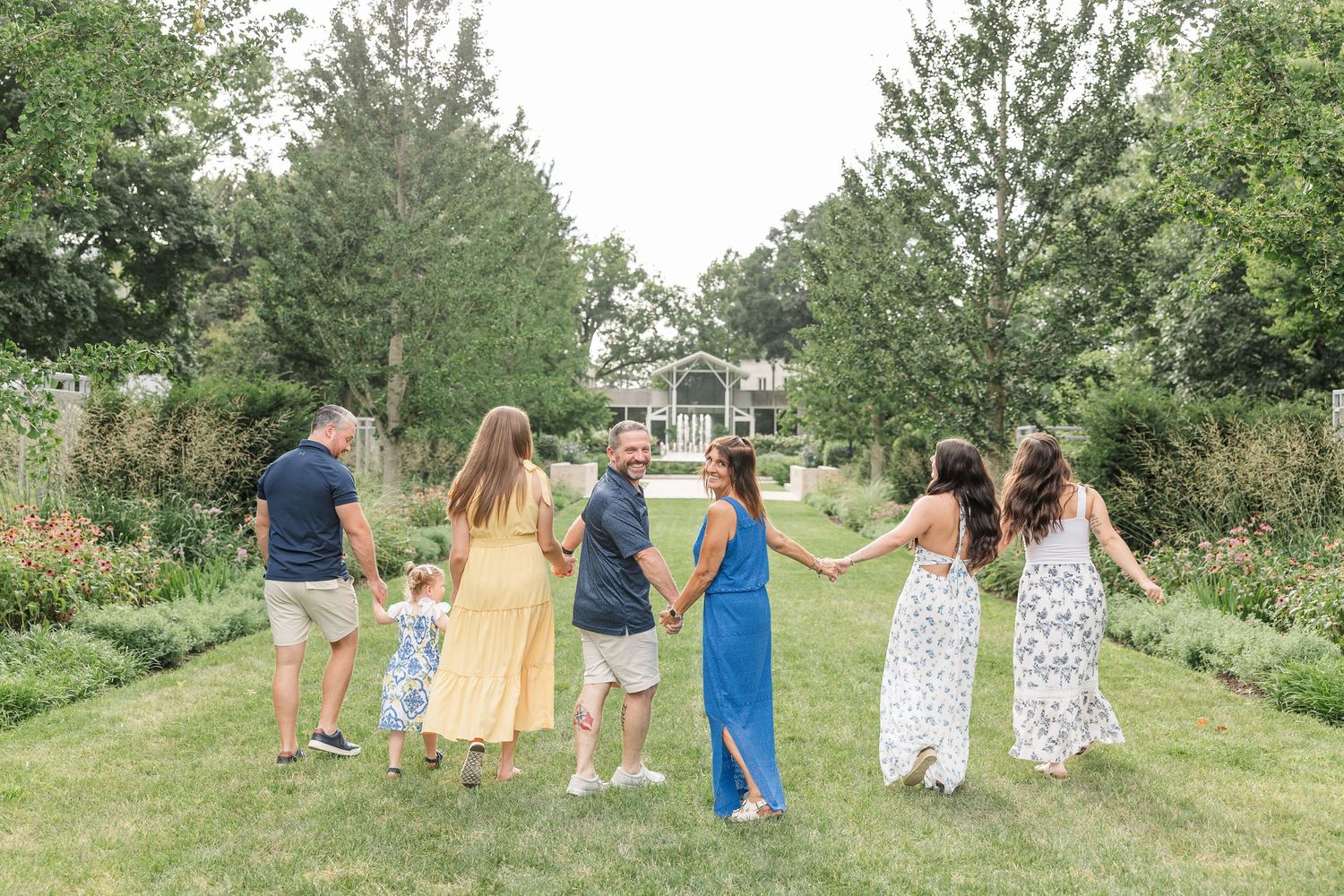 Family group holding hands walking through a lush green garden path together.
