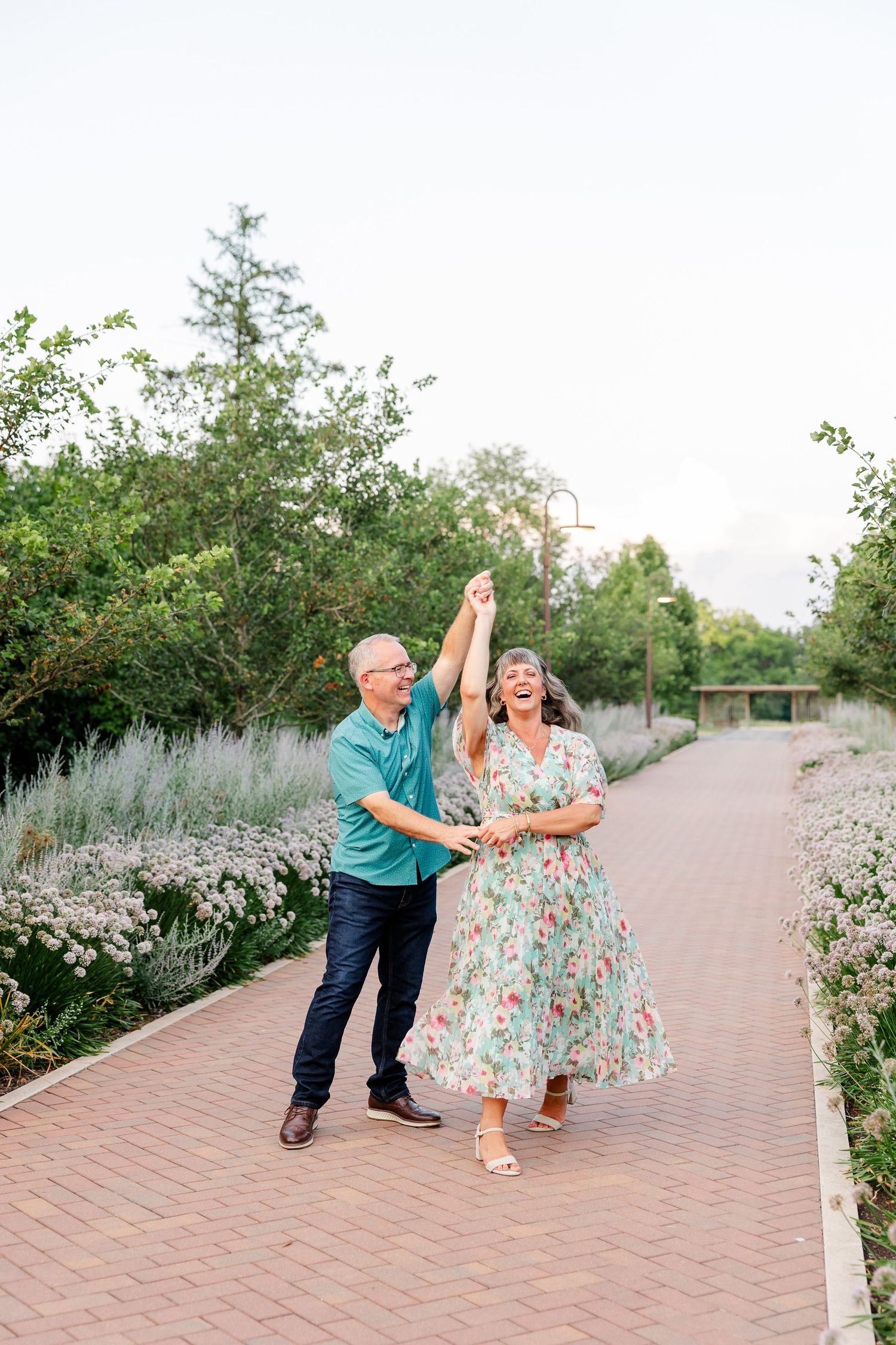 Joyful couple dancing on a brick garden path surrounded by lush greenery and wildflowers.