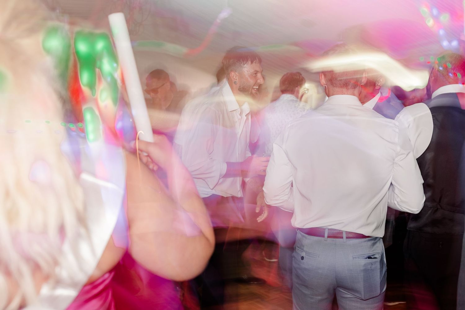 Energetic blurred motion shot of guests dancing at lively wedding reception under white tent.