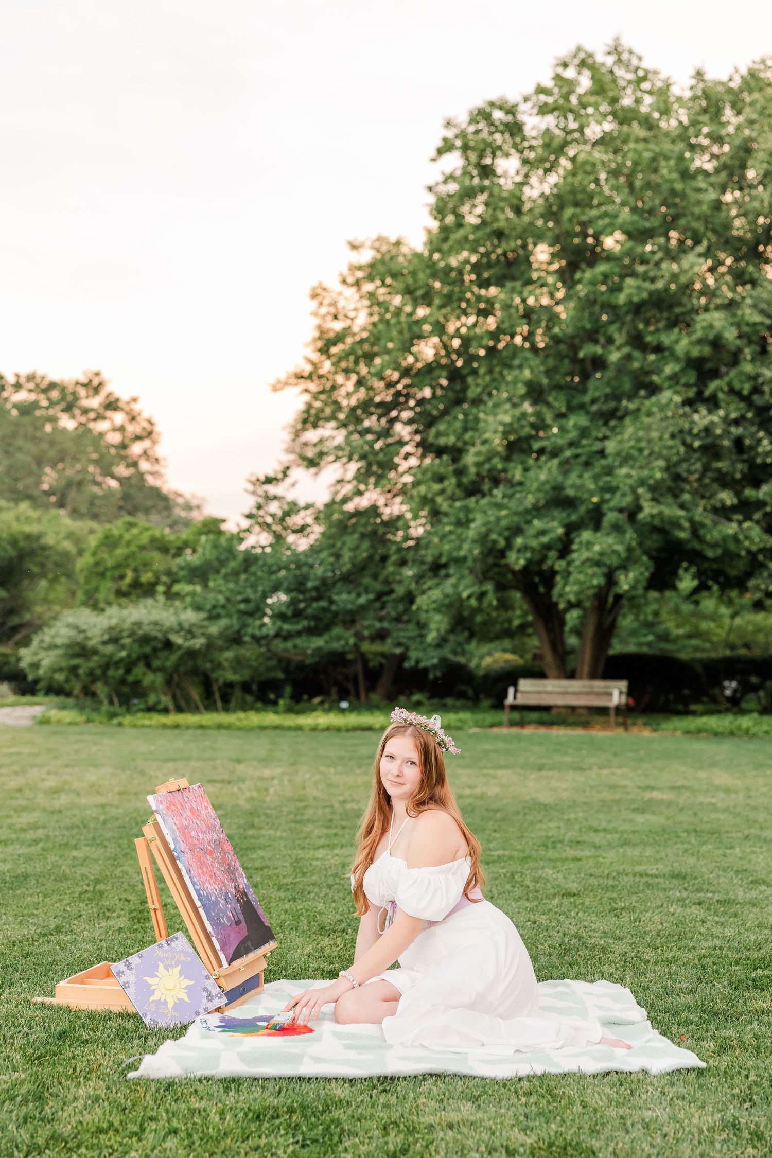 Artistic senior portrait of Samantha sitting beside her easel and painting on the lawn at Cantigny Park.