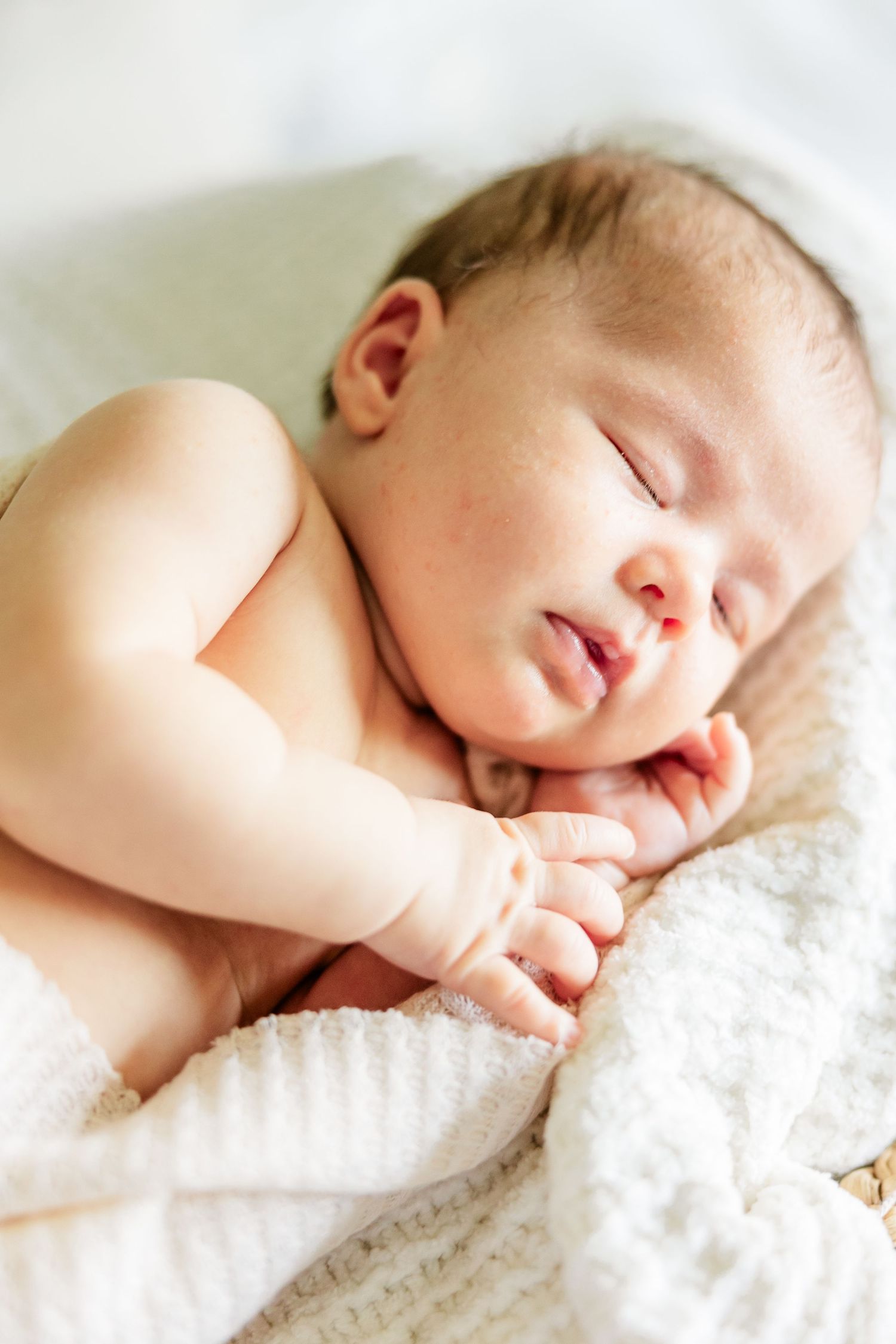 Sleeping newborn baby girl curled up on a blanket during a lifestyle newborn session at home