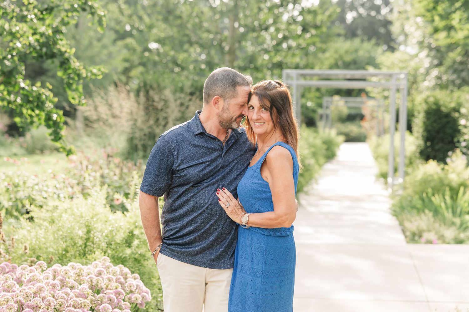 A loving couple shares a tender moment on a garden path surrounded by blooming flowers.