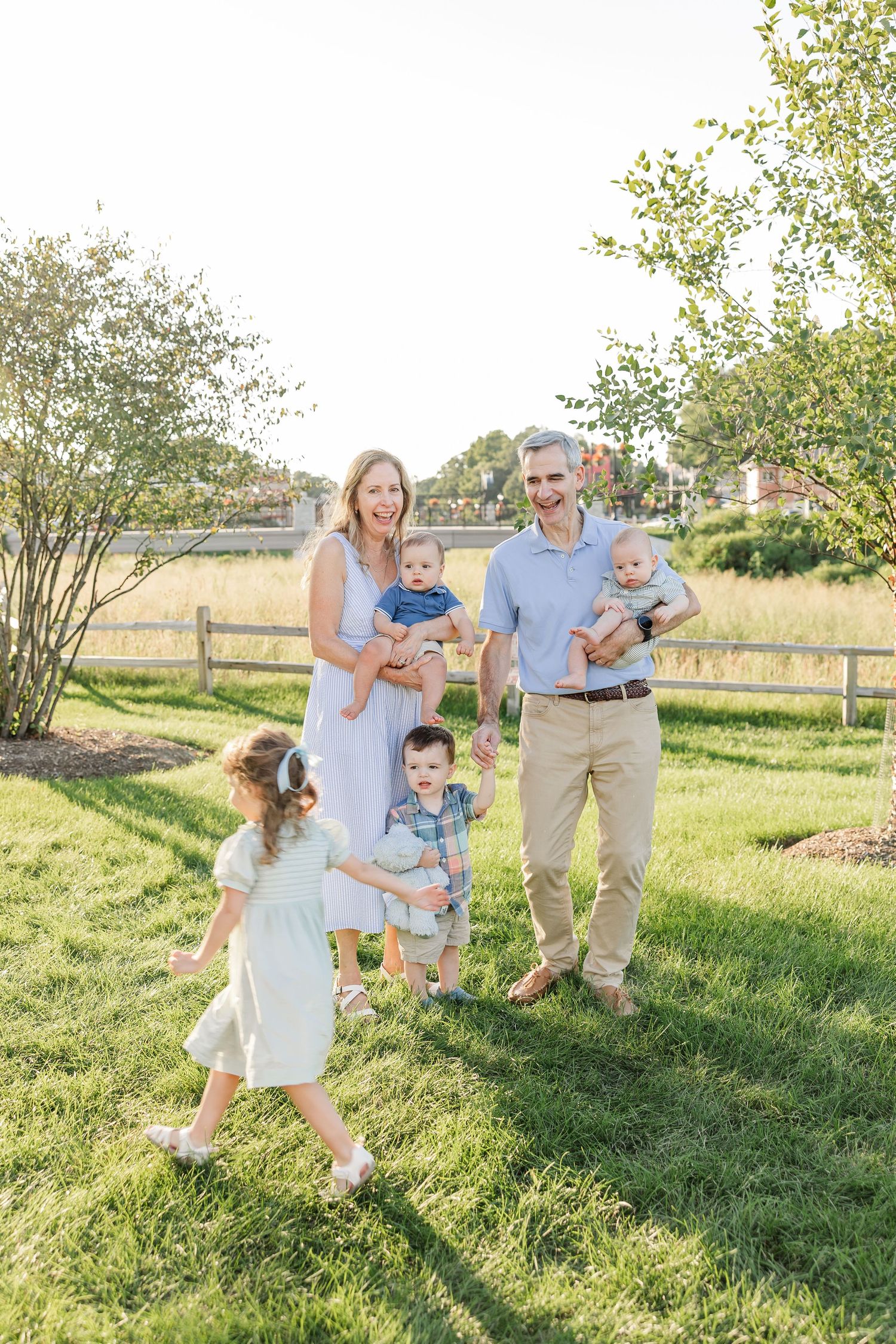 A joyful family with three young children walks together on lush green grass during a sunny outdoor photo session.