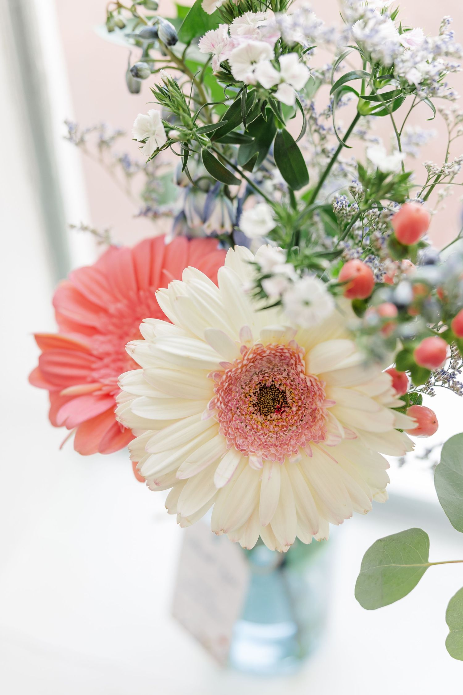 Close-up of white and coral gerbera daisies with eucalyptus and berries in a wedding bouquet.