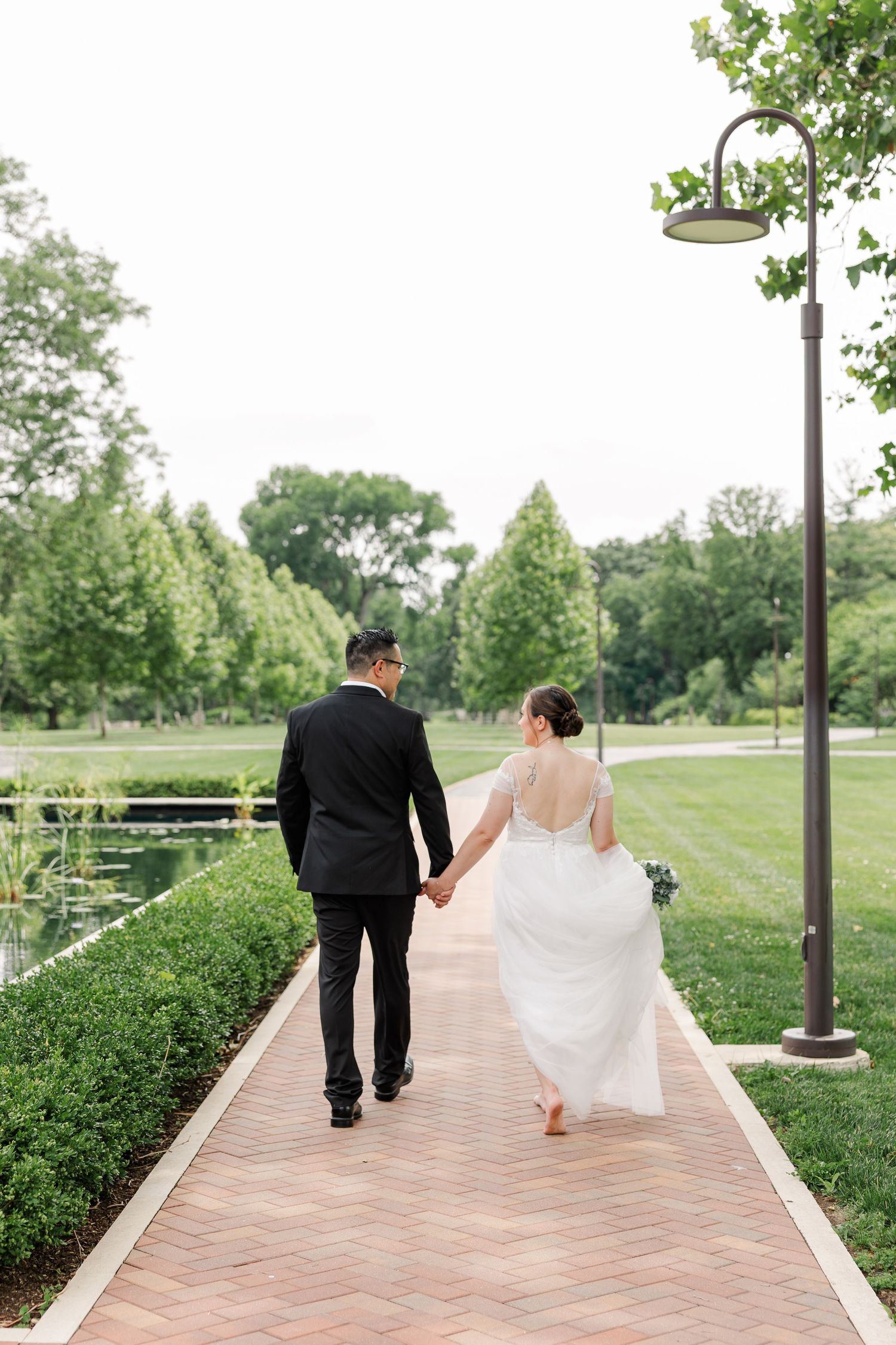 Monika and Rafael walking hand in hand along a brick path through the formal gardens at Cantigny Park.