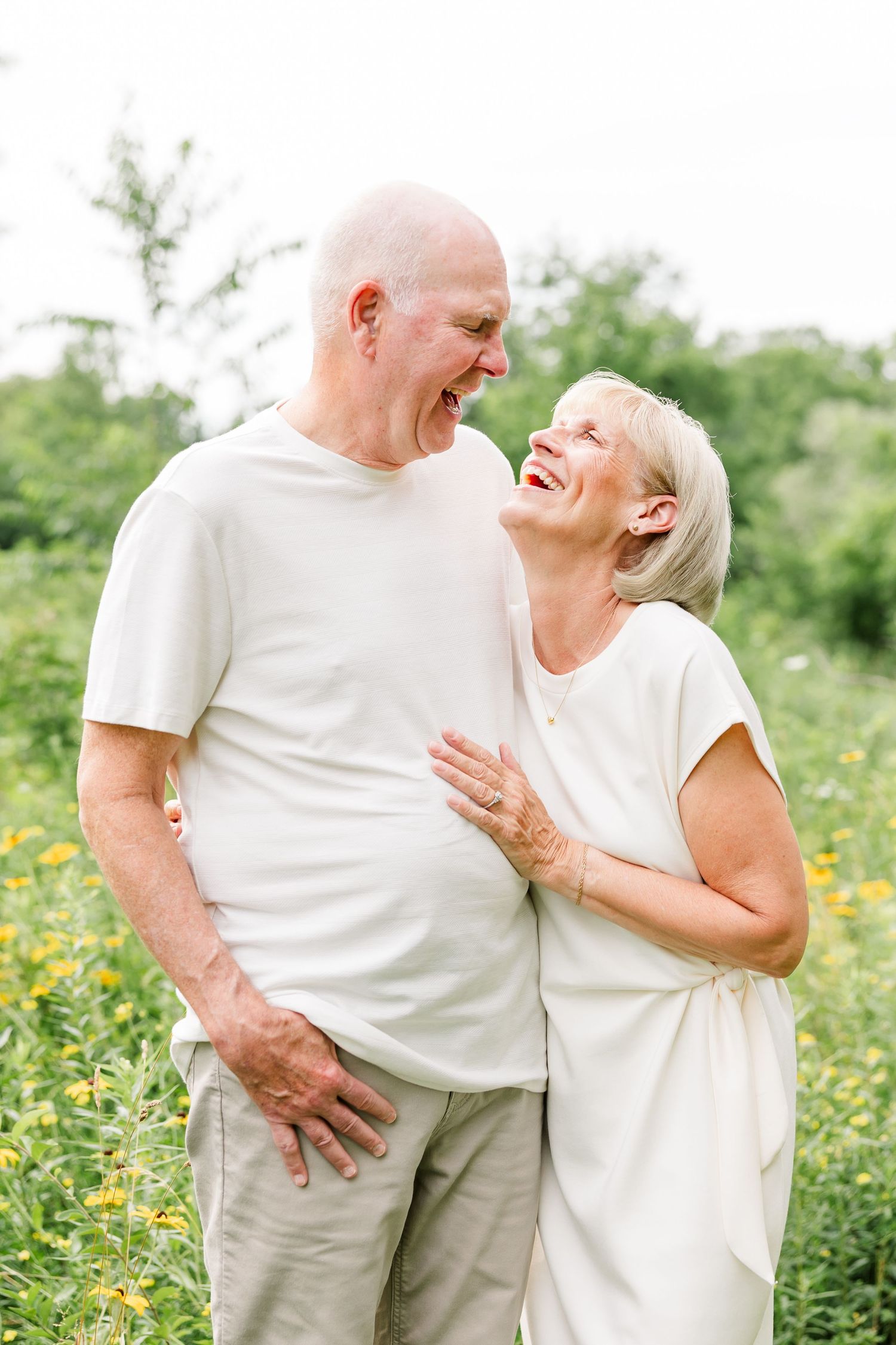 Happy senior couple laughing together in a sunny field of yellow flowers outdoors.