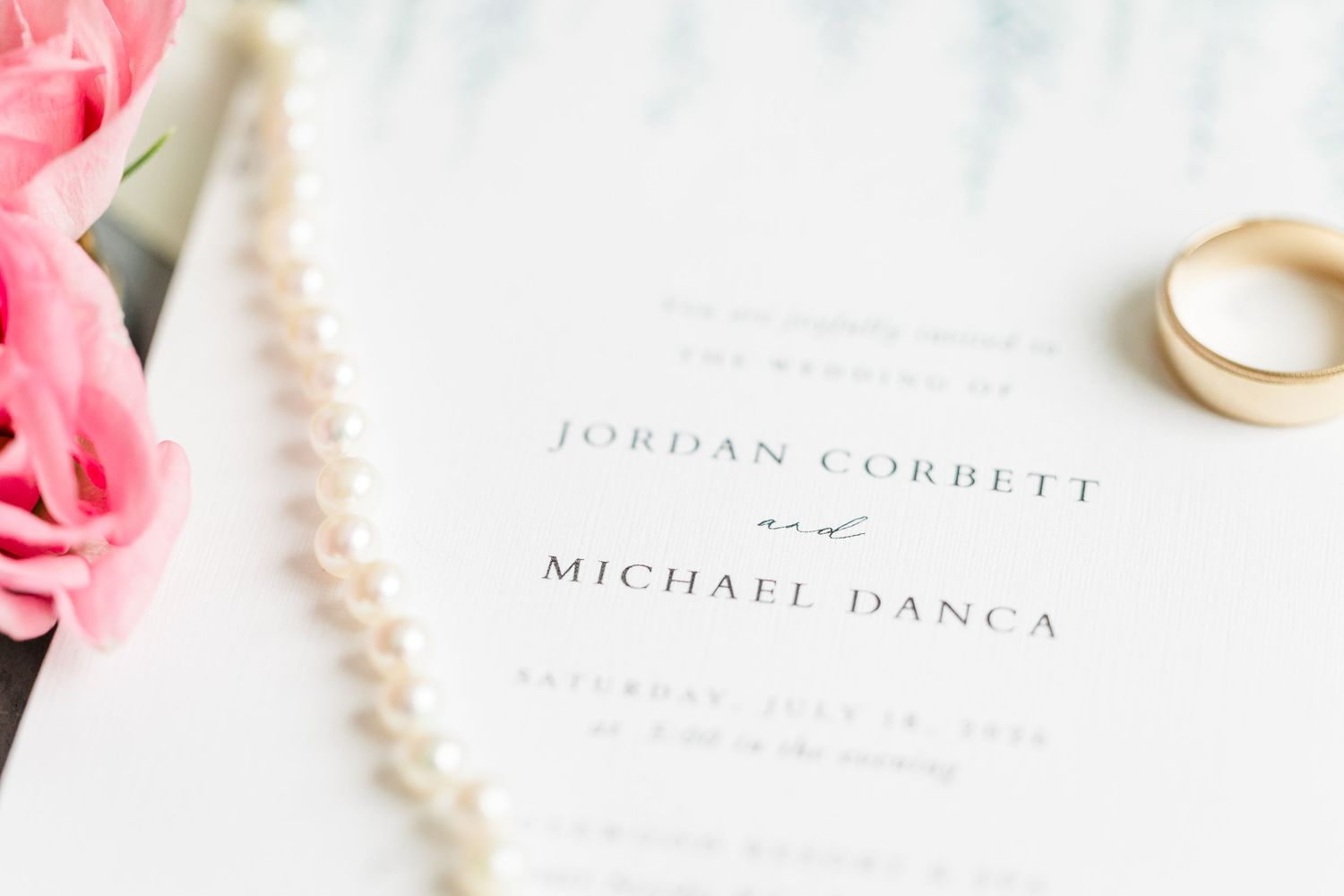 Wedding invitation for Jordan Corbett and Michael Danca with pearl necklace and gold ring on white background.