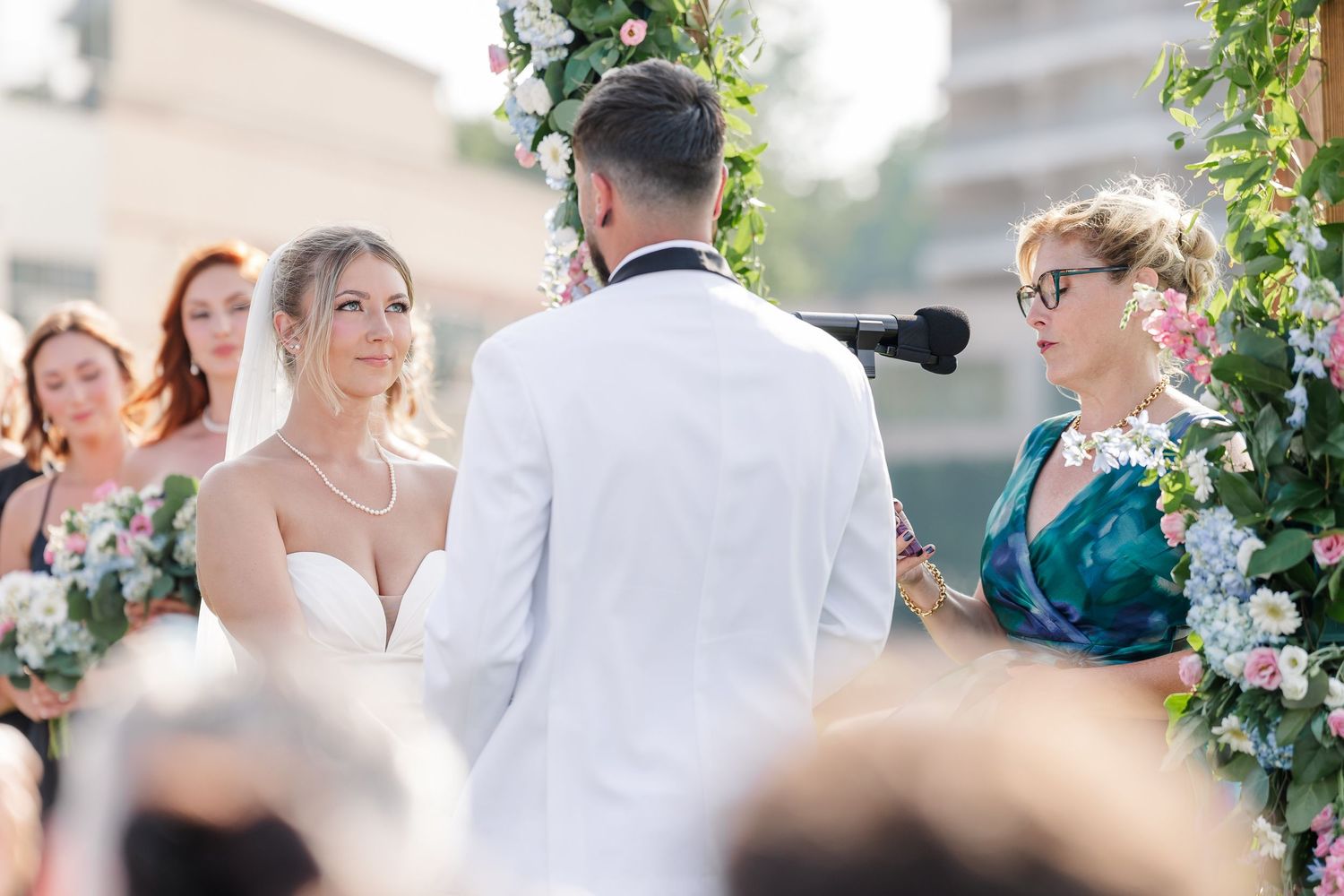 Bride and groom exchanging vows at floral arch with officiant during outdoor wedding.
