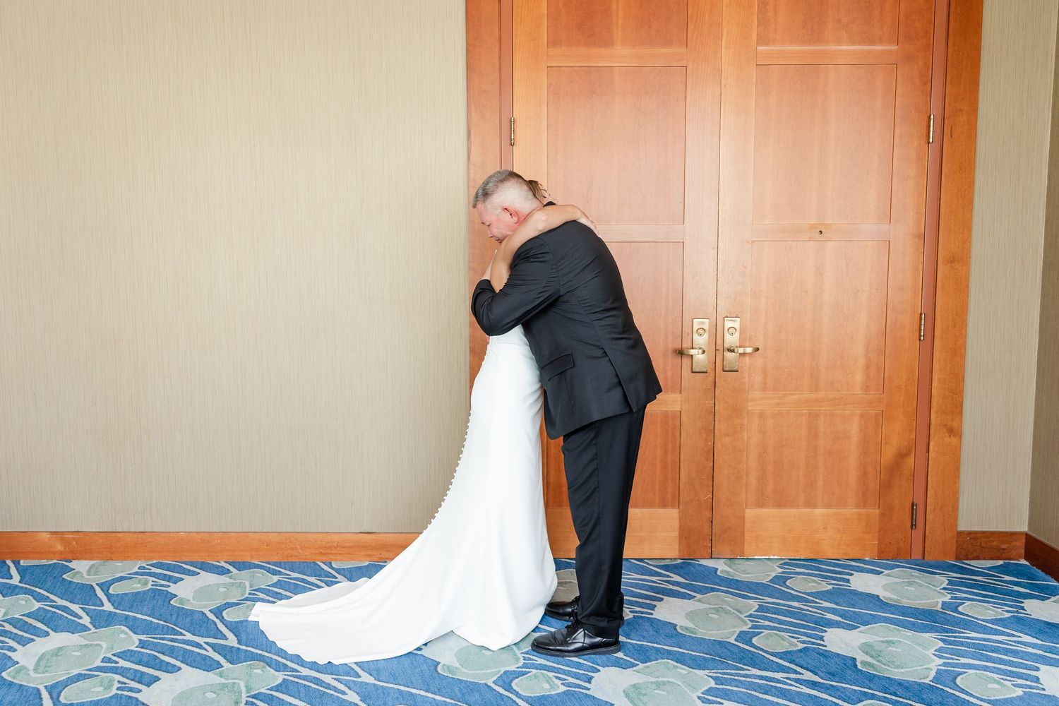 Father of the bride sharing an emotional hug with his daughter in her white wedding gown before the ceremony.