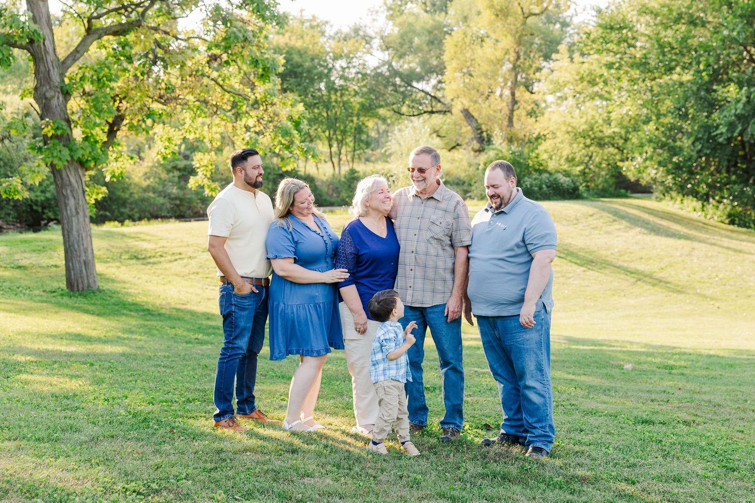 A group of people in color-coordinated blue and gray outfits pose together on a grassy hill during a sunny day.Sorg family portraits at Sham