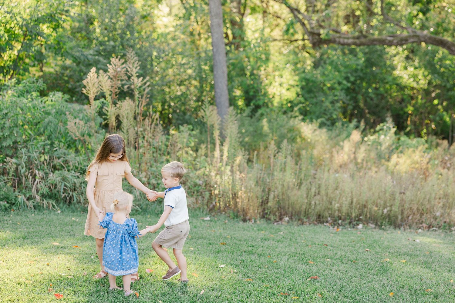 Two children in blue outfits play together in a lush green summer field at sunset.