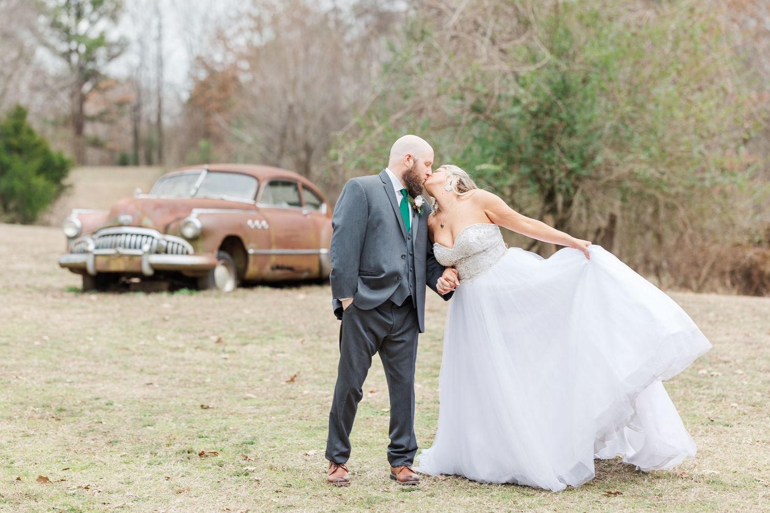 Playful wedding moment captured outdoors with vintage car backdrop.