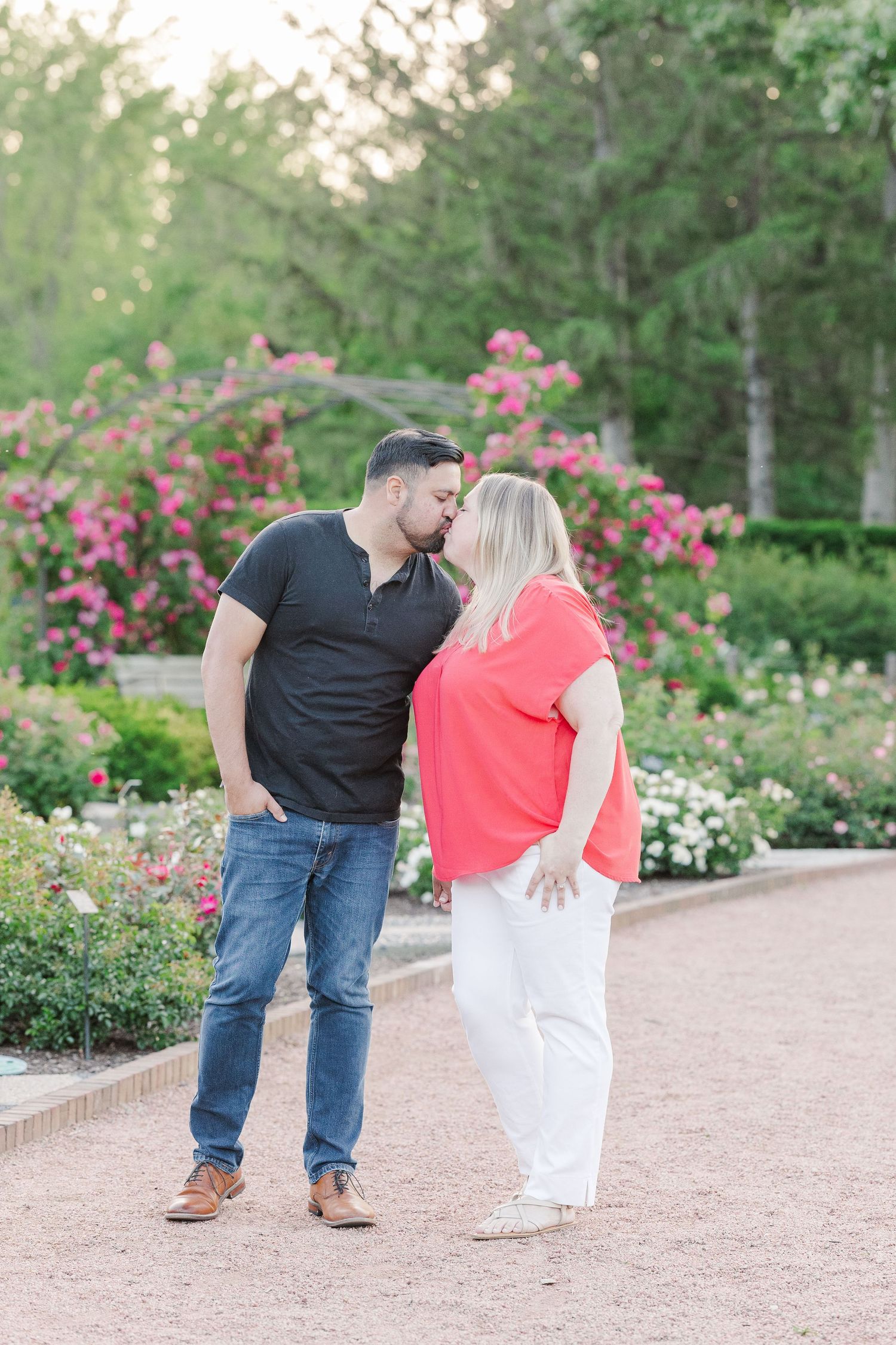 Intimate moment between couple on garden path with pink flowering bushes in background.