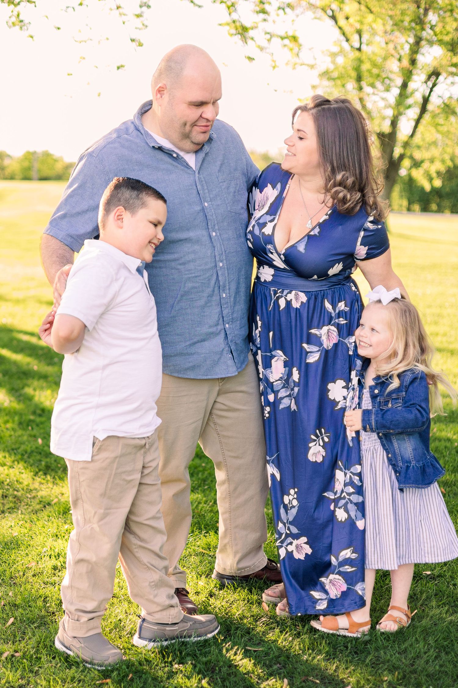 A family poses together outdoors in coordinated blue and white outfits on a sunny day in a grassy field.