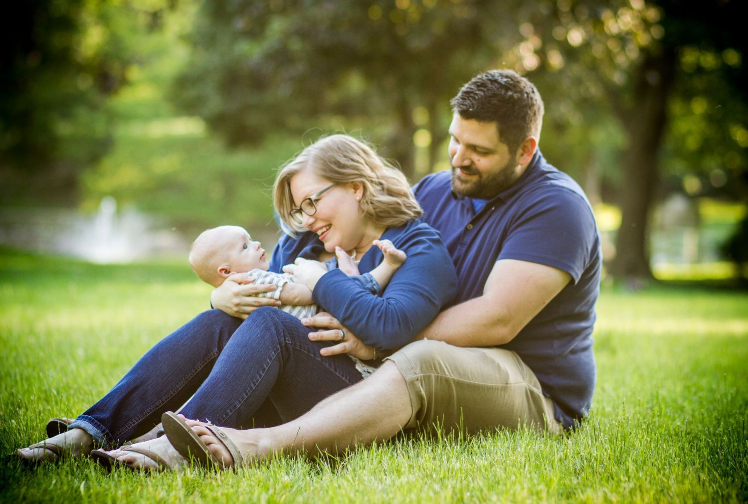 Family sitting together on grass in a sunny park.