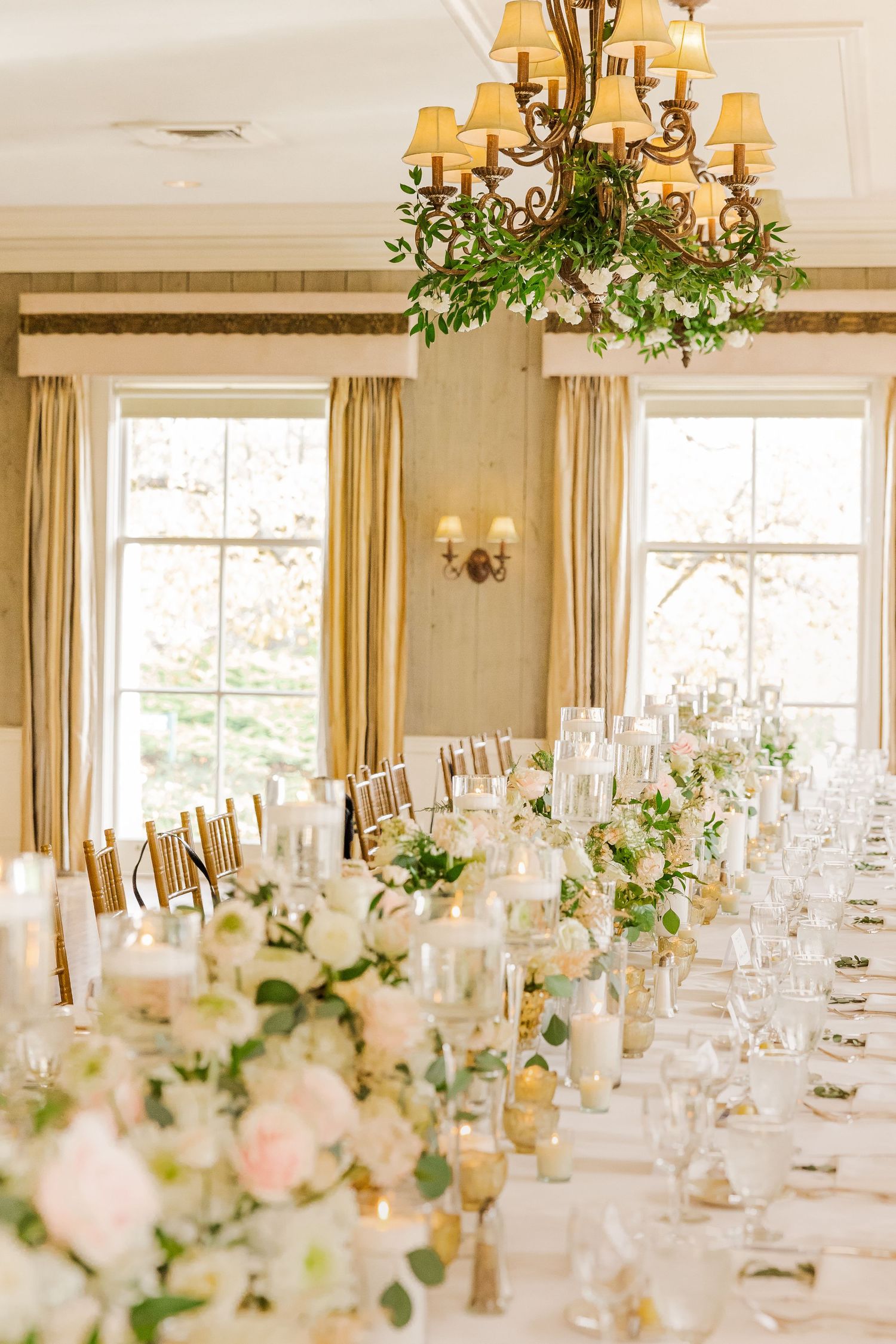 Bright reception room with chandeliers and long tables decorated with white and blush floral arrangements.