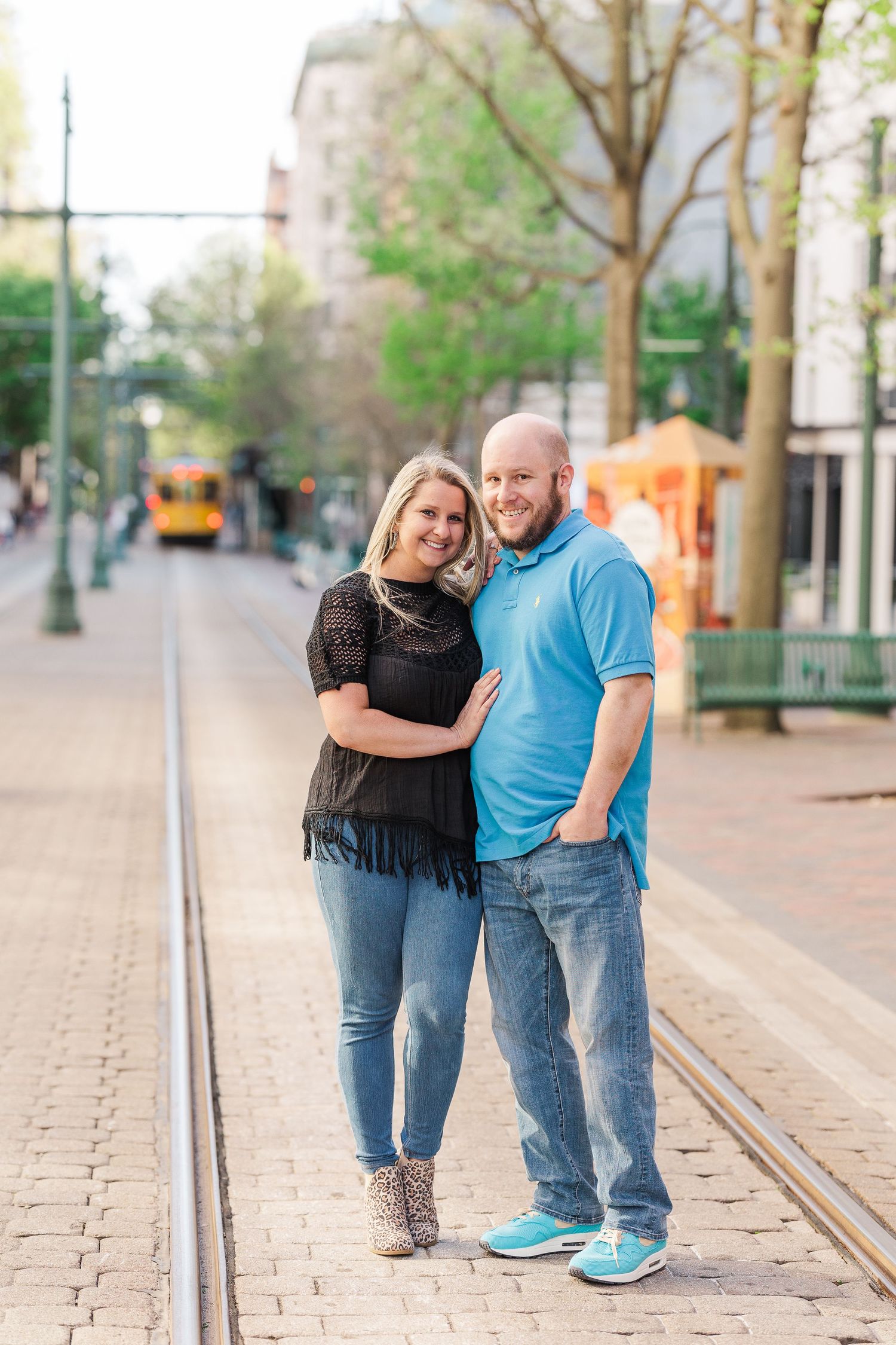 A couple poses together on trolley tracks during a sunny afternoon photoshoot.