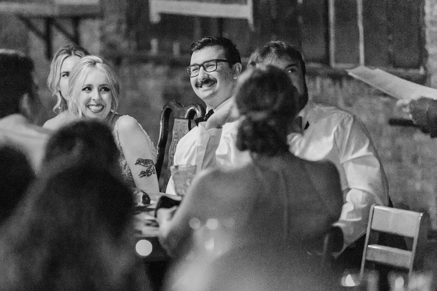 Black and white candid reception photo capturing joyful moment among guests.