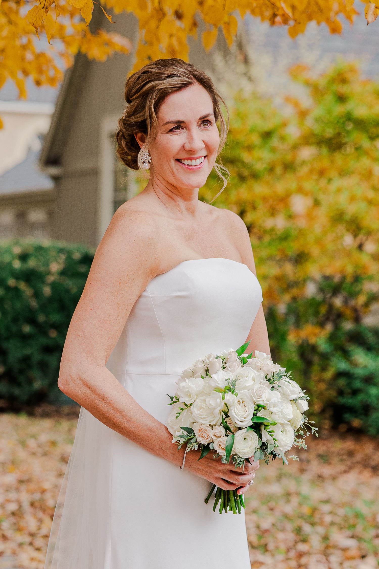 Beautiful autumn wedding portrait featuring a strapless white gown and classic white rose bouquet against fall foliage.