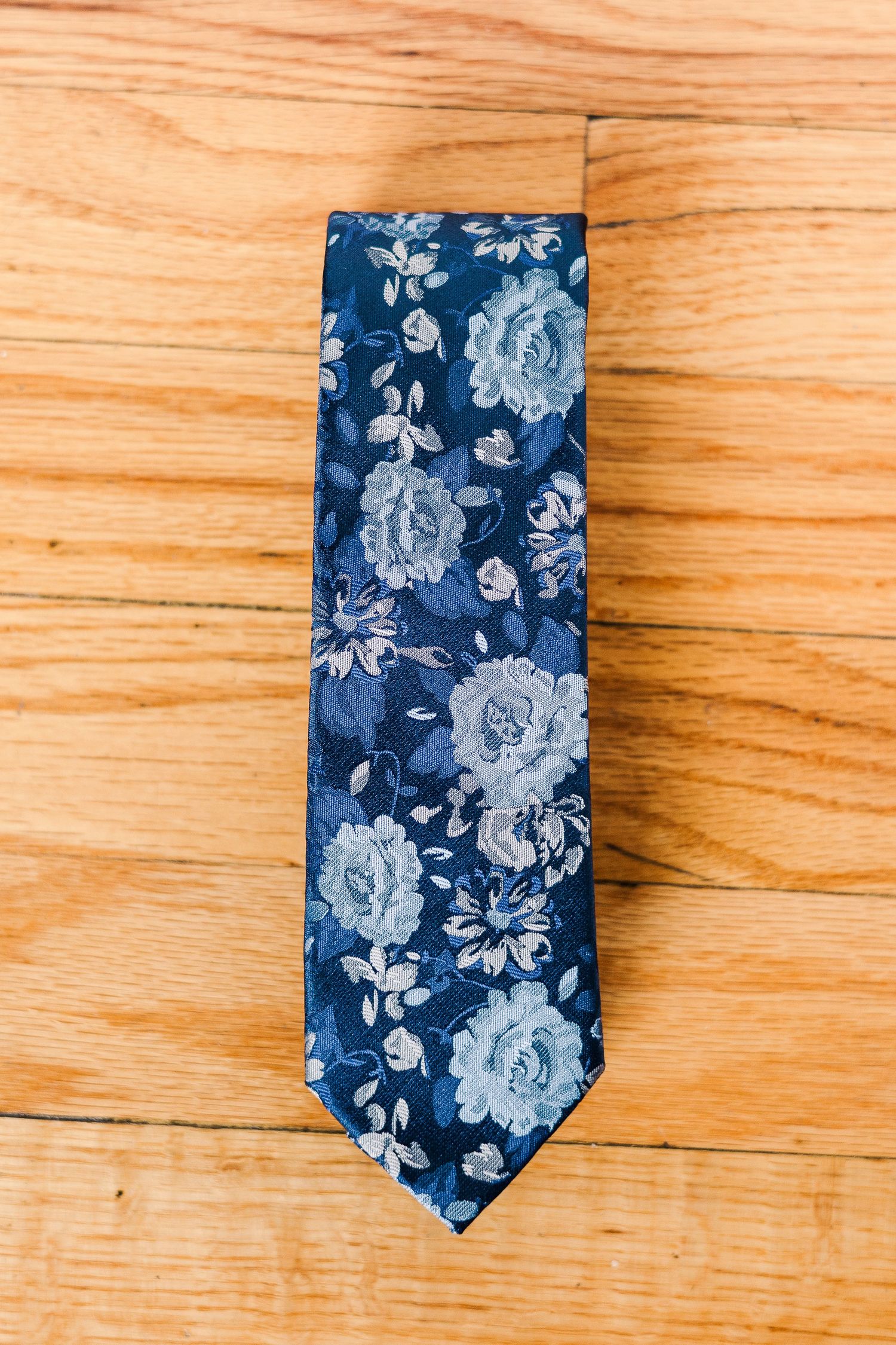 Navy blue floral tie with light blue rose pattern on wooden surface.