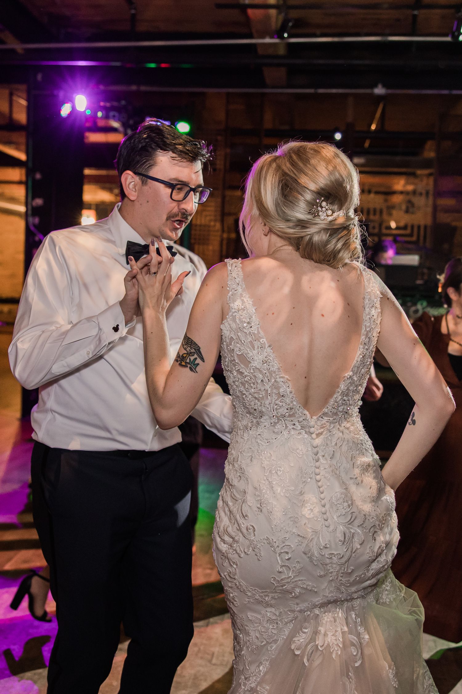 Wedding couple dancing under purple stage lights in reception venue.