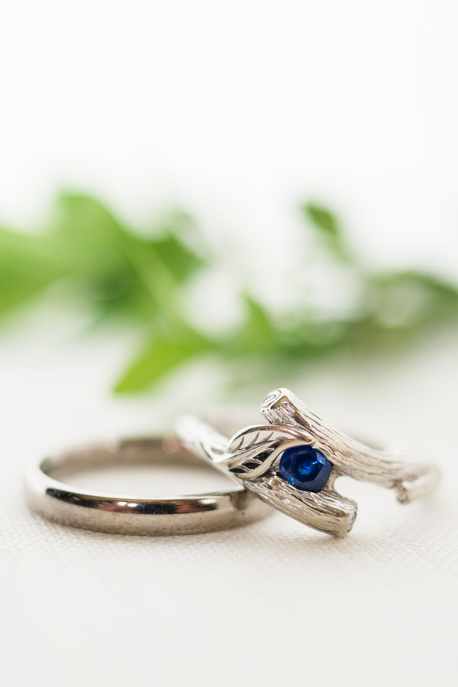 Close-up of wedding bands with a sapphire engagement ring against white background.