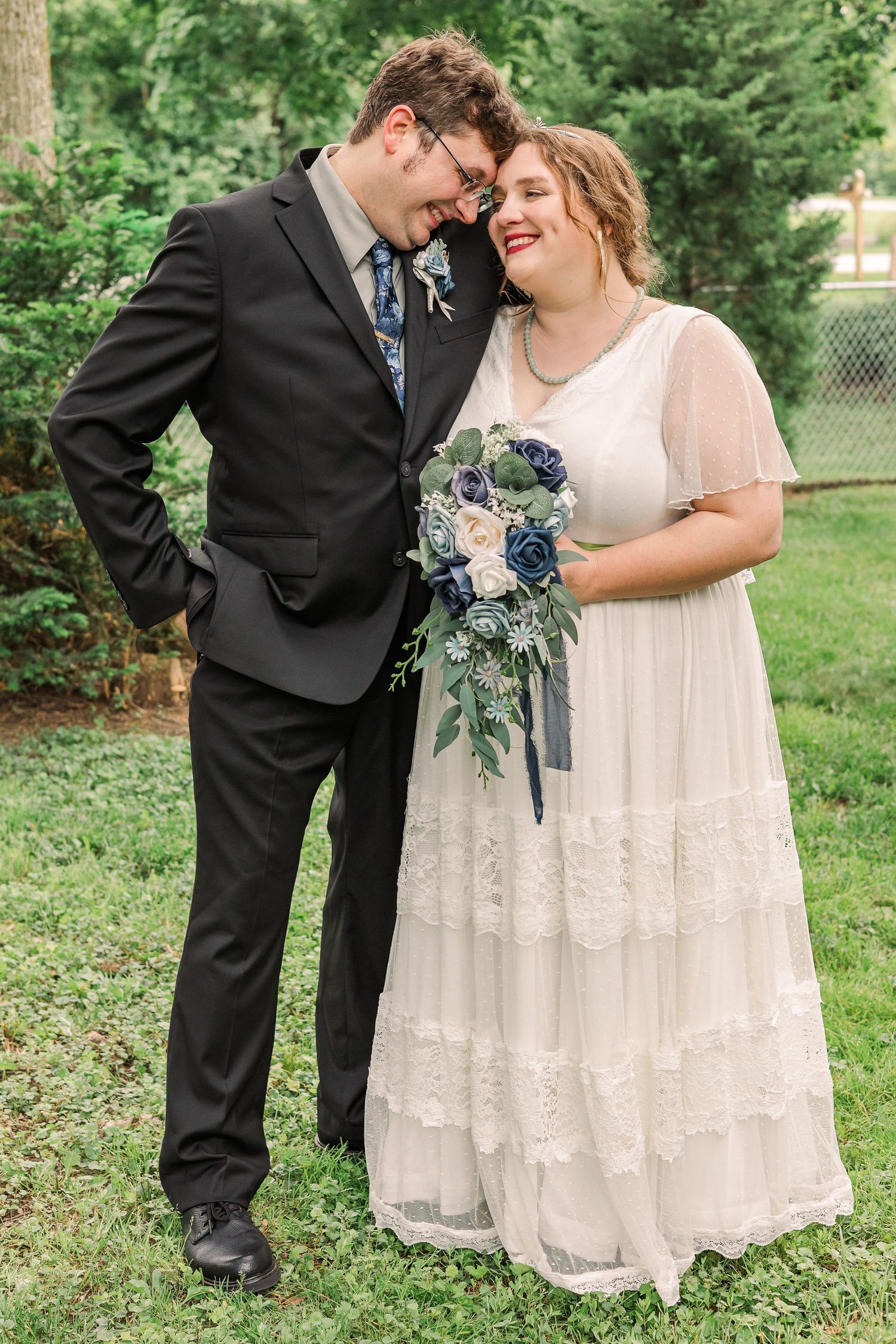 A joyful wedding portrait with the couple laughing together while holding a blue and white floral bouquet.