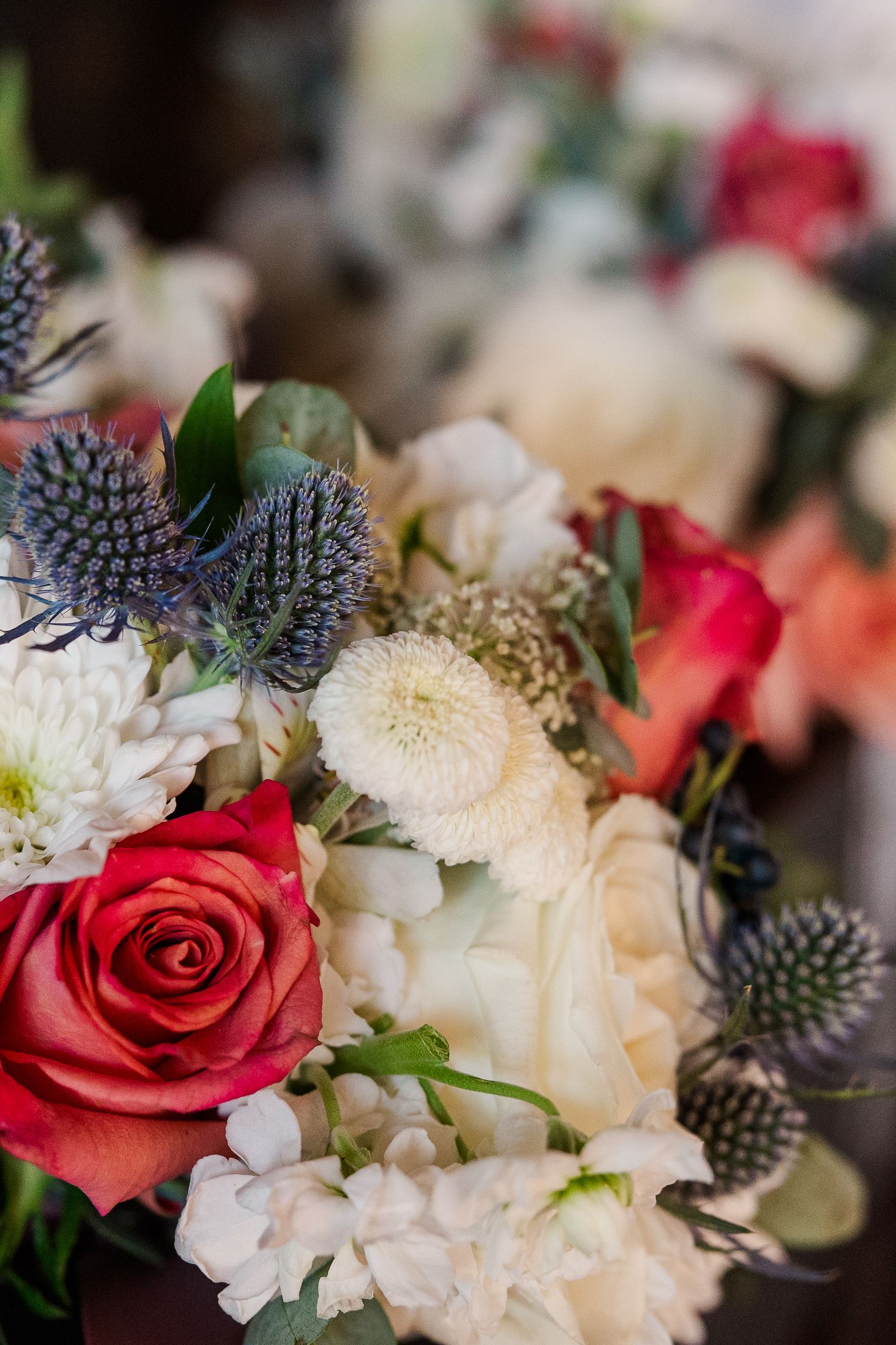 Beautiful wedding bouquet featuring red roses, white chrysanthemums, and blue thistle flowers in a romantic arrangement.