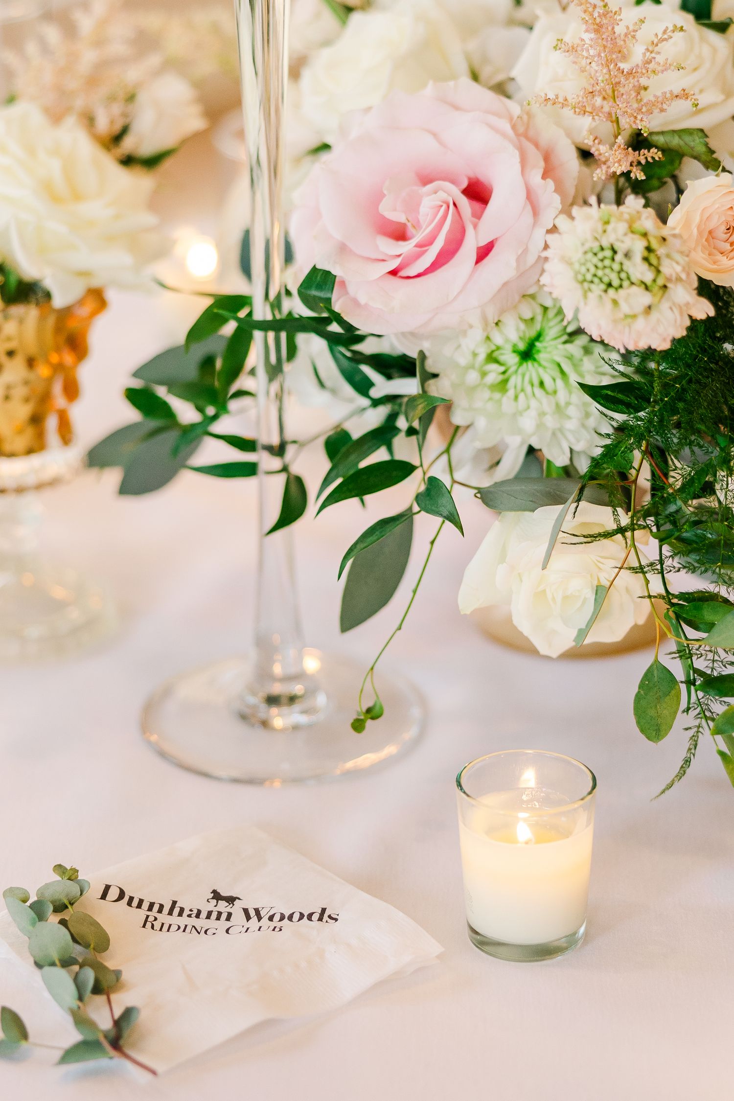 Wedding reception table detail with pink roses, candles and Dunham Woods place card on white linens.
