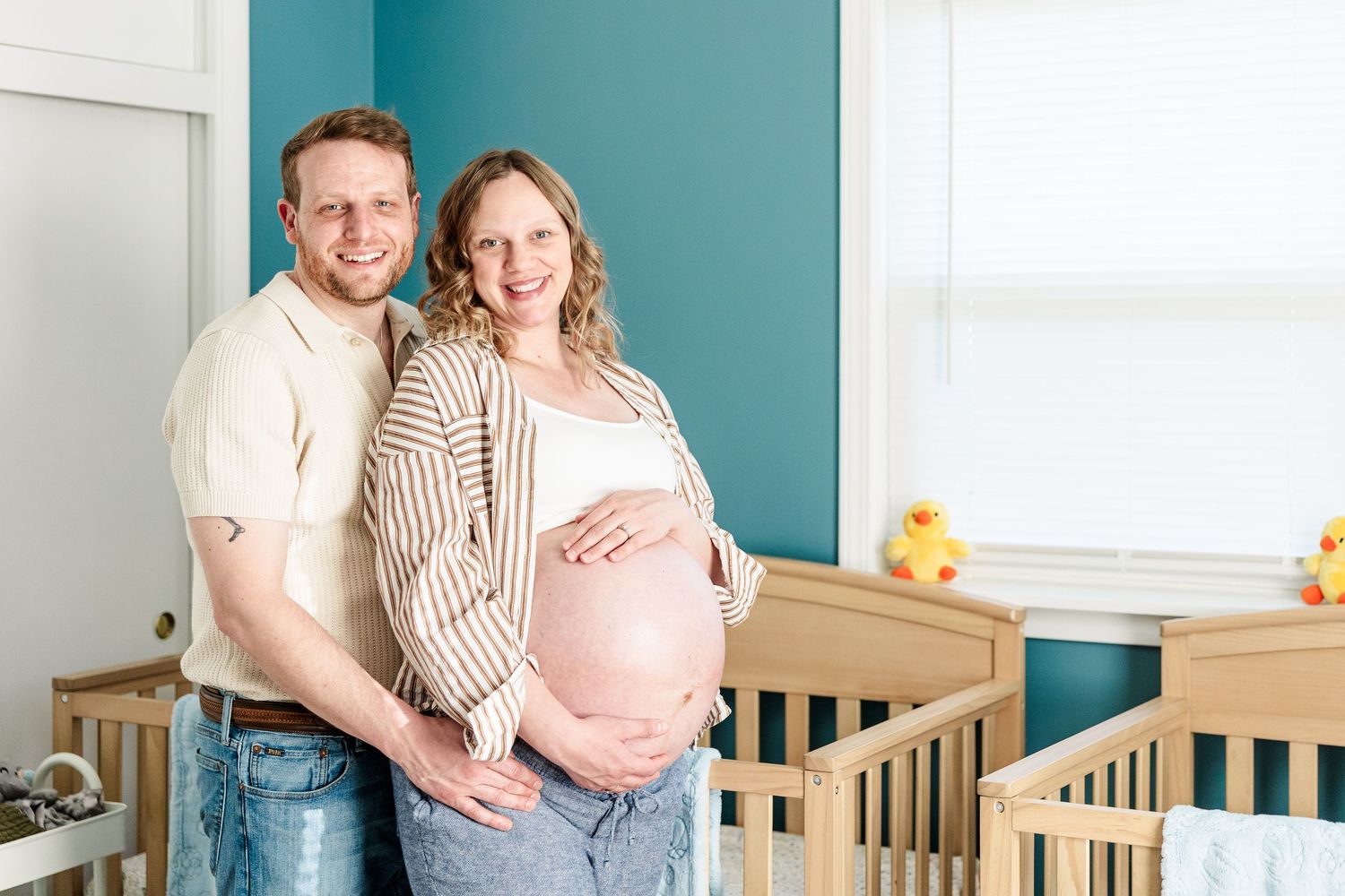Expecting parents holding baby bump in twin nursery during an in-home maternity session in Crystal Lake.