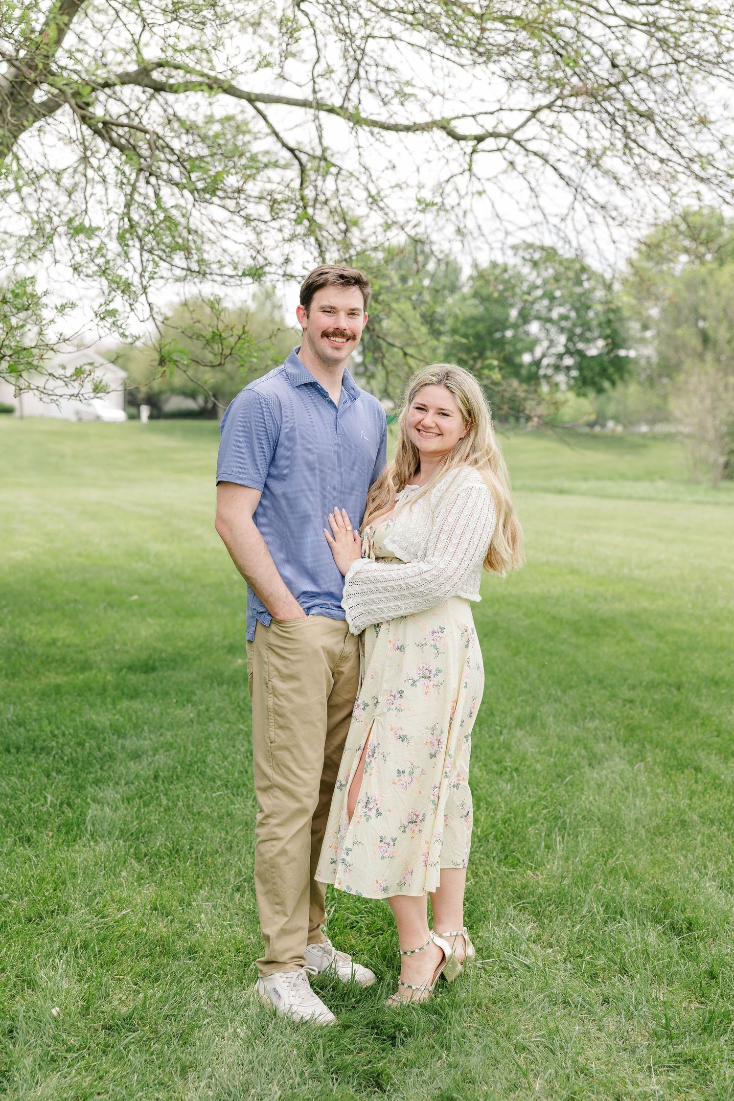 A smiling couple embraces under a blooming tree on a lush green lawn during a spring outdoor portrait session.