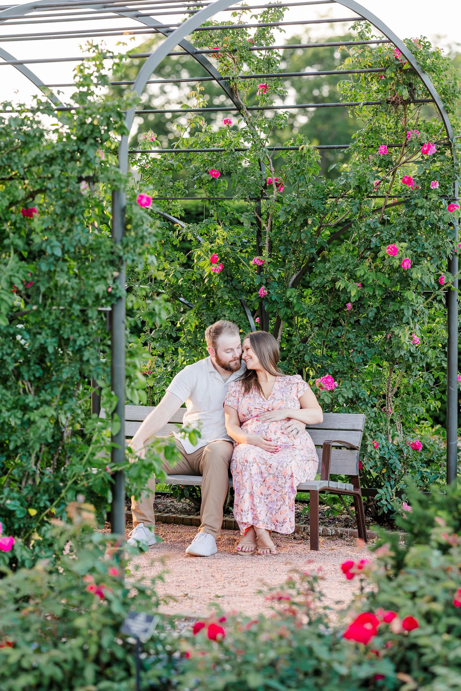 Expecting parents seated beneath a rose arch during a garden maternity session at Cantigny Park in Wheaton Illinois