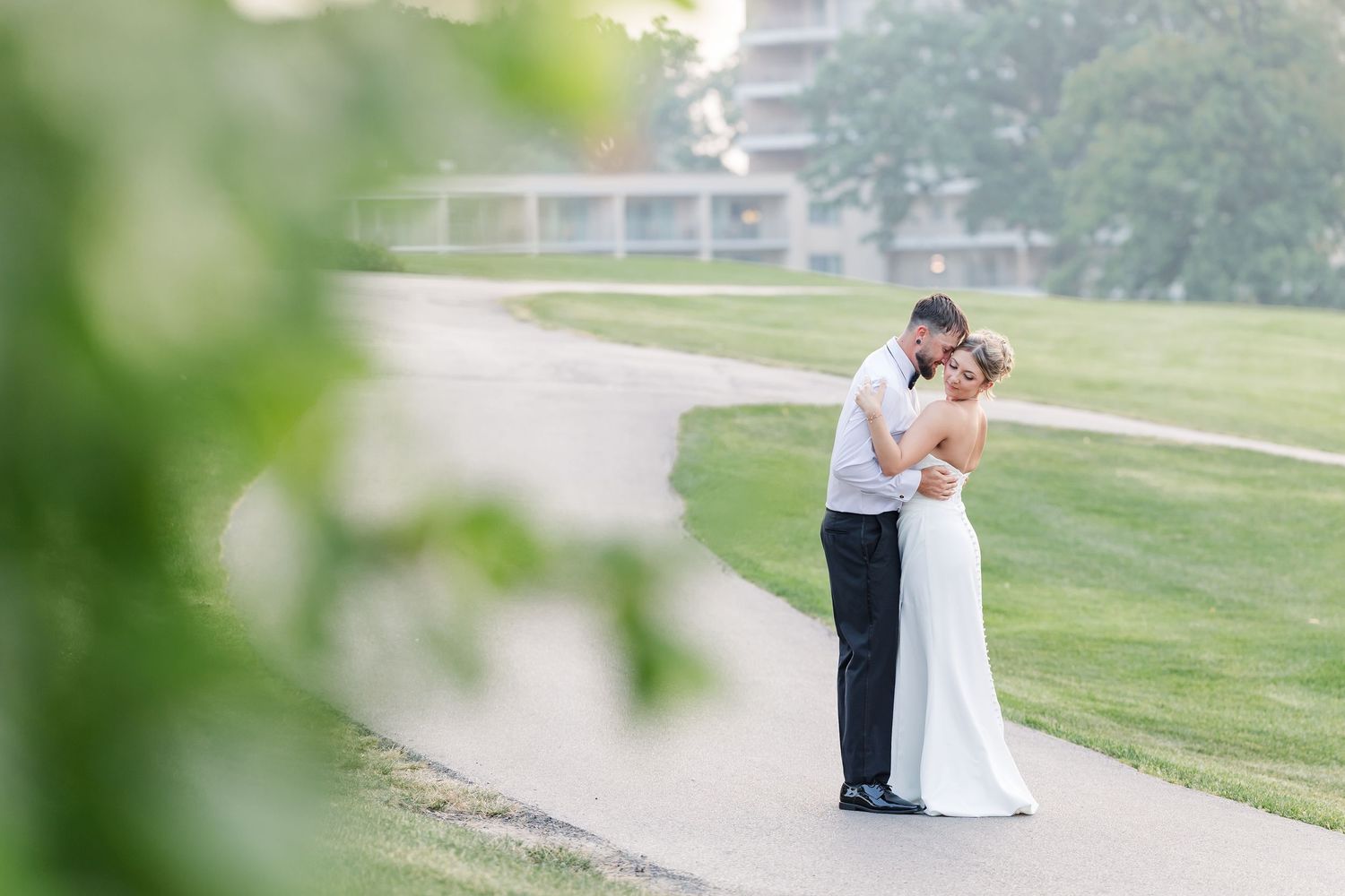 Bride and groom embracing on misty golf course path surrounded by green trees and lawn.
