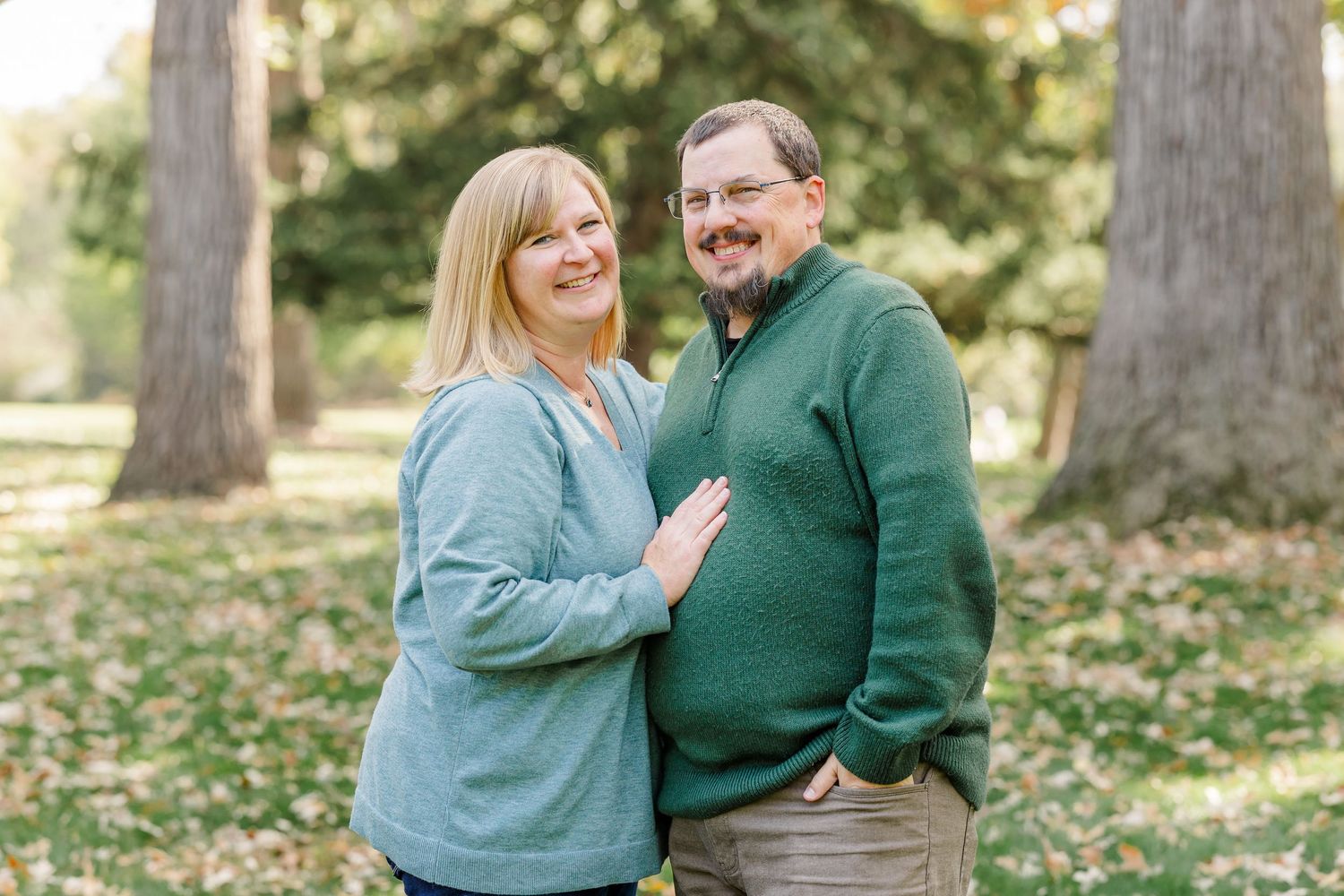 Smiling couple poses together among autumn trees in a park setting.
