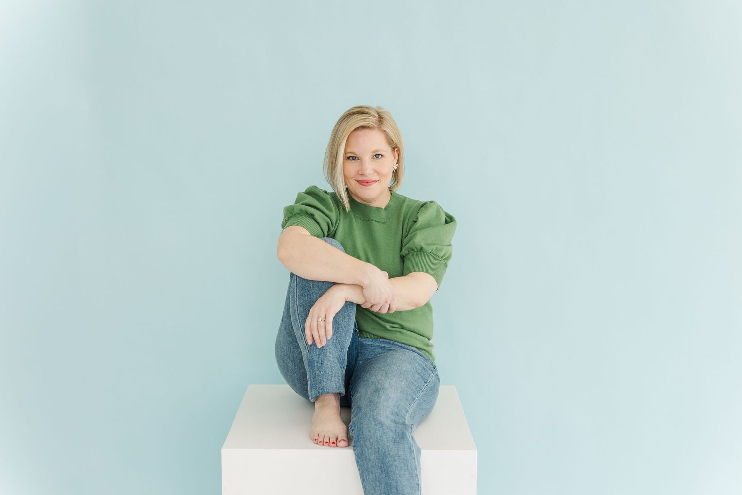 Person in casual attire sitting comfortably against light blue studio backdrop.