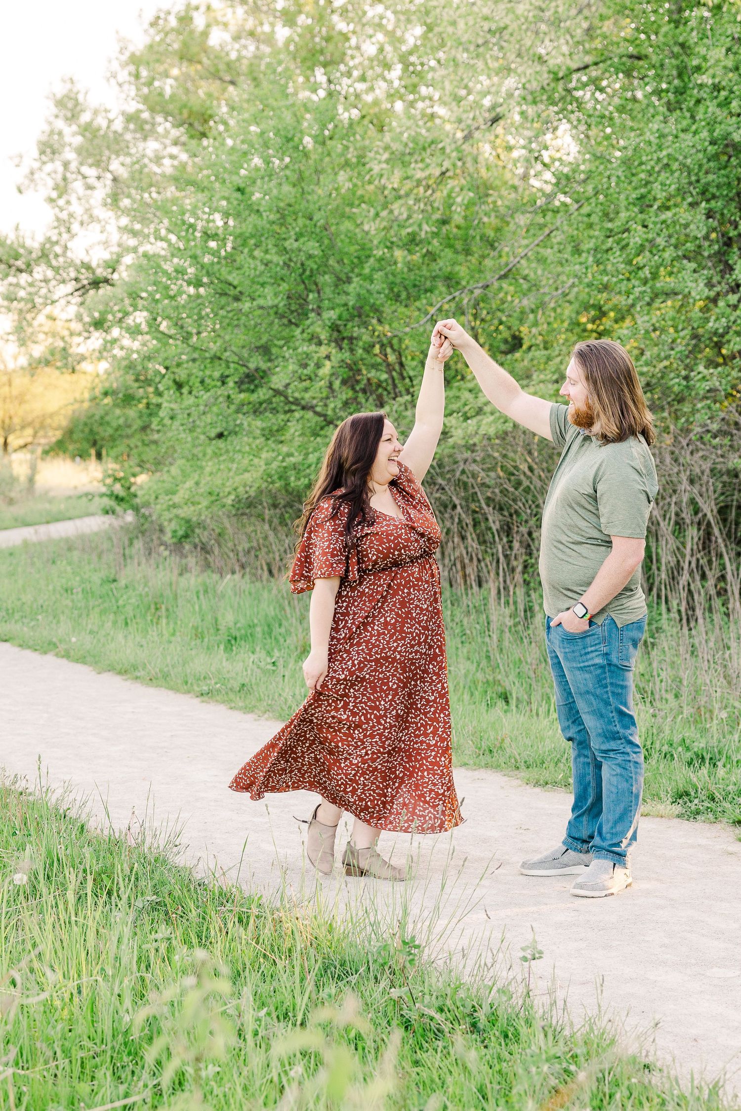 A couple dancing and twirling together on a nature path surrounded by lush greenery.