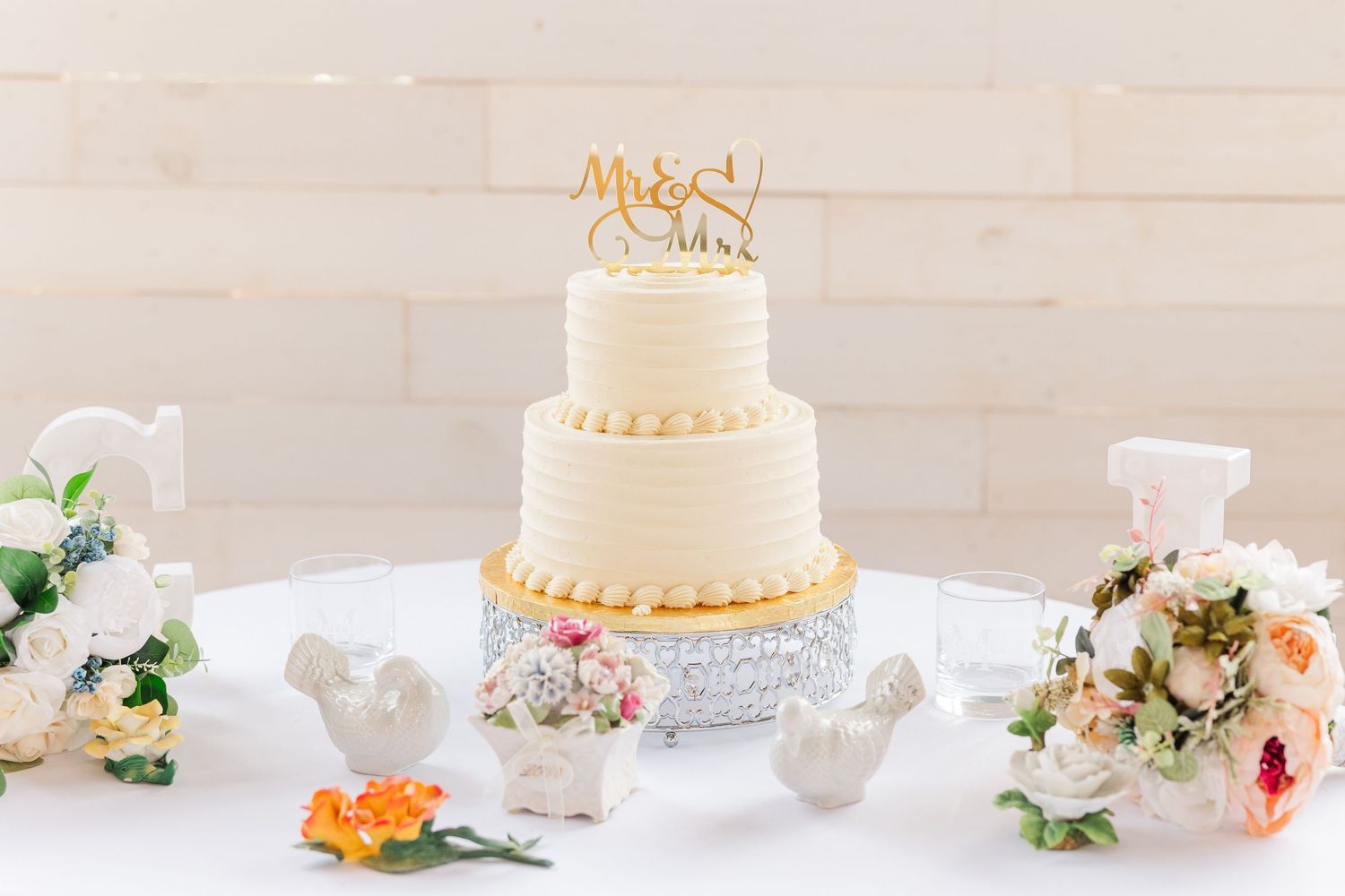 Elegant three-tier white wedding cake with gold topper and floral decorations on crystal stand.