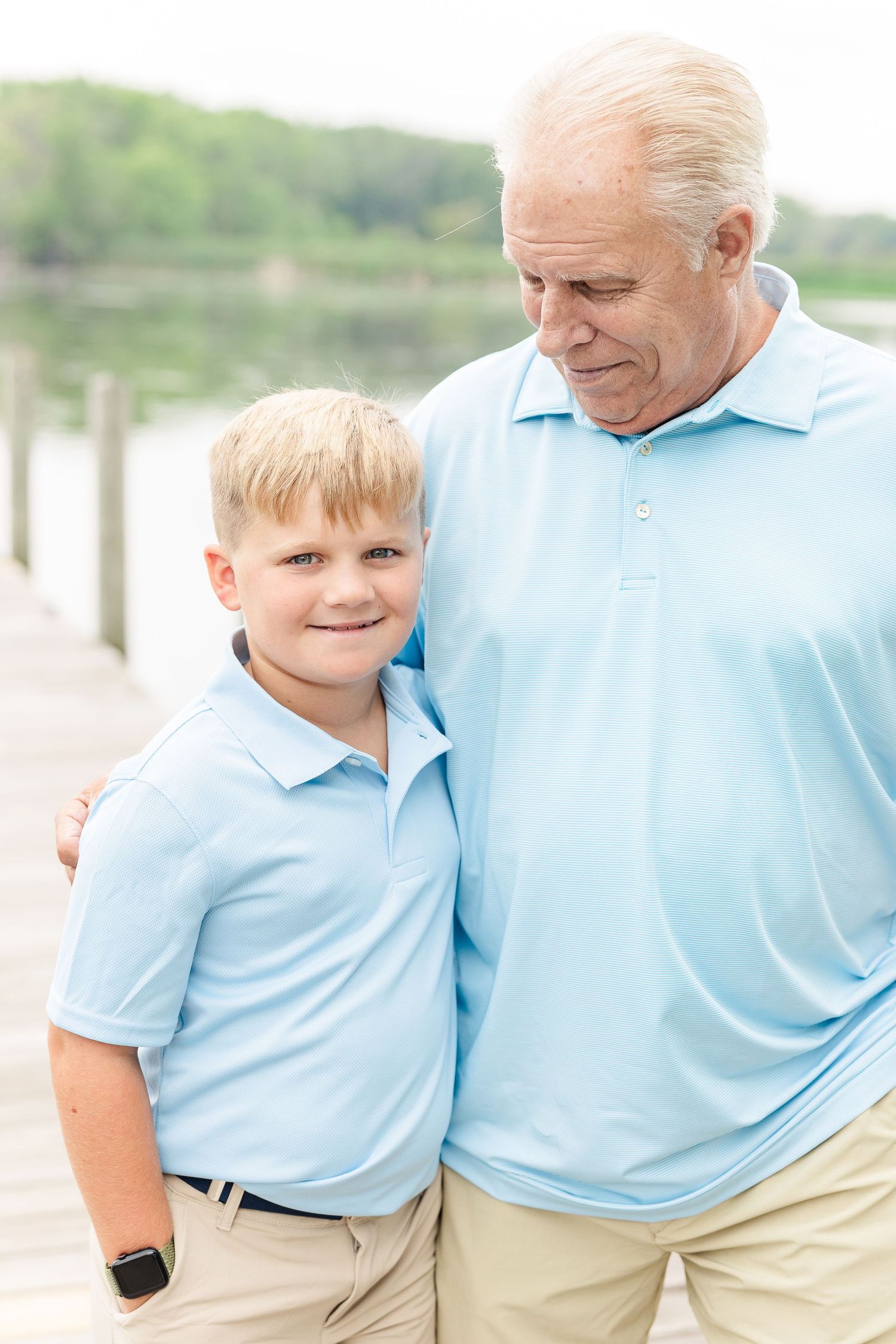A loving outdoor portrait of two generations in matching light blue polo shirts by the water.