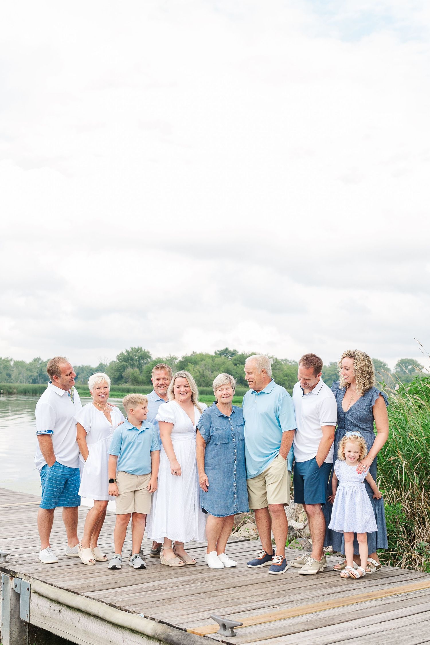 Multi-generational family poses on lakeside dock wearing coordinated white and blue outfits.