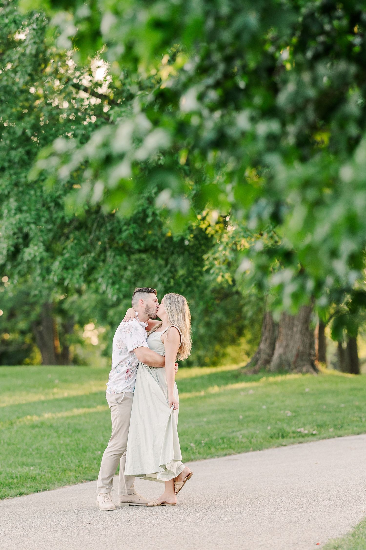 A couple shares a tender embrace on a tree-lined path at sunset.