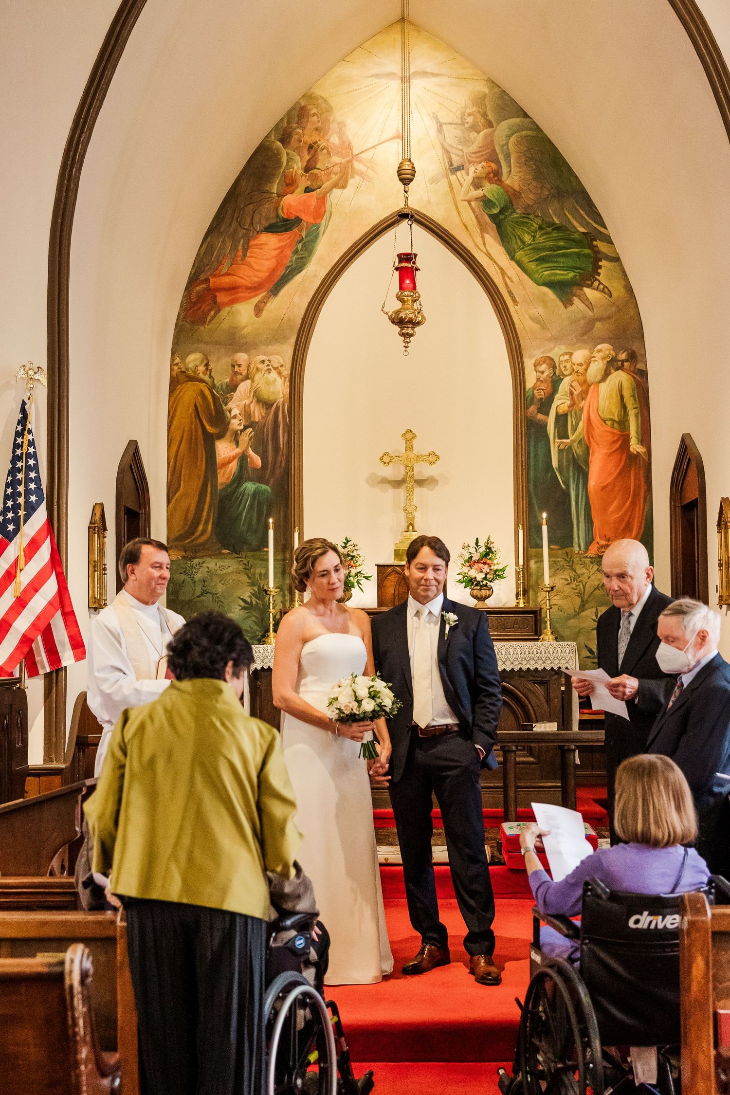 Interior of small chapel with religious murals and American flag during wedding ceremony.