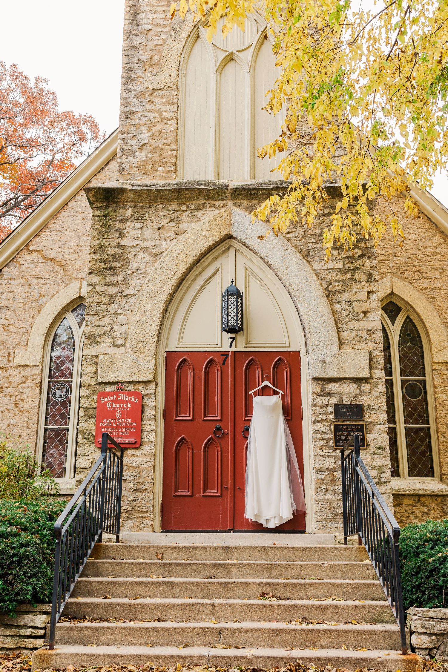 Historic stone church entrance with red door and autumn leaves in golden light.