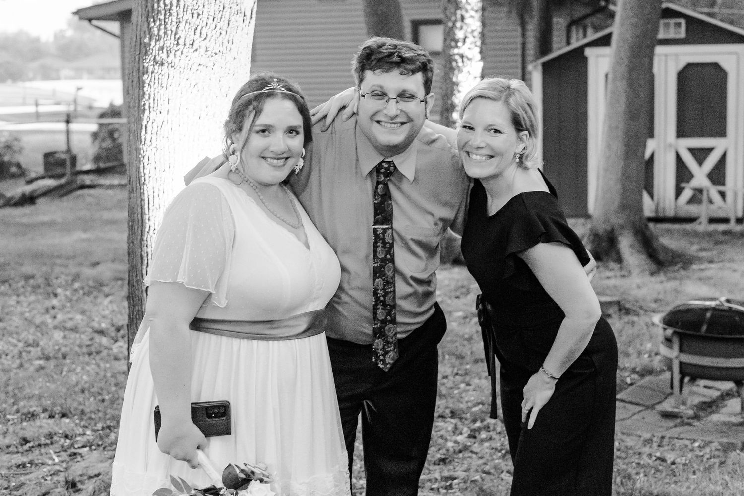 Wedding party poses together outside rustic barn in black and white photo.