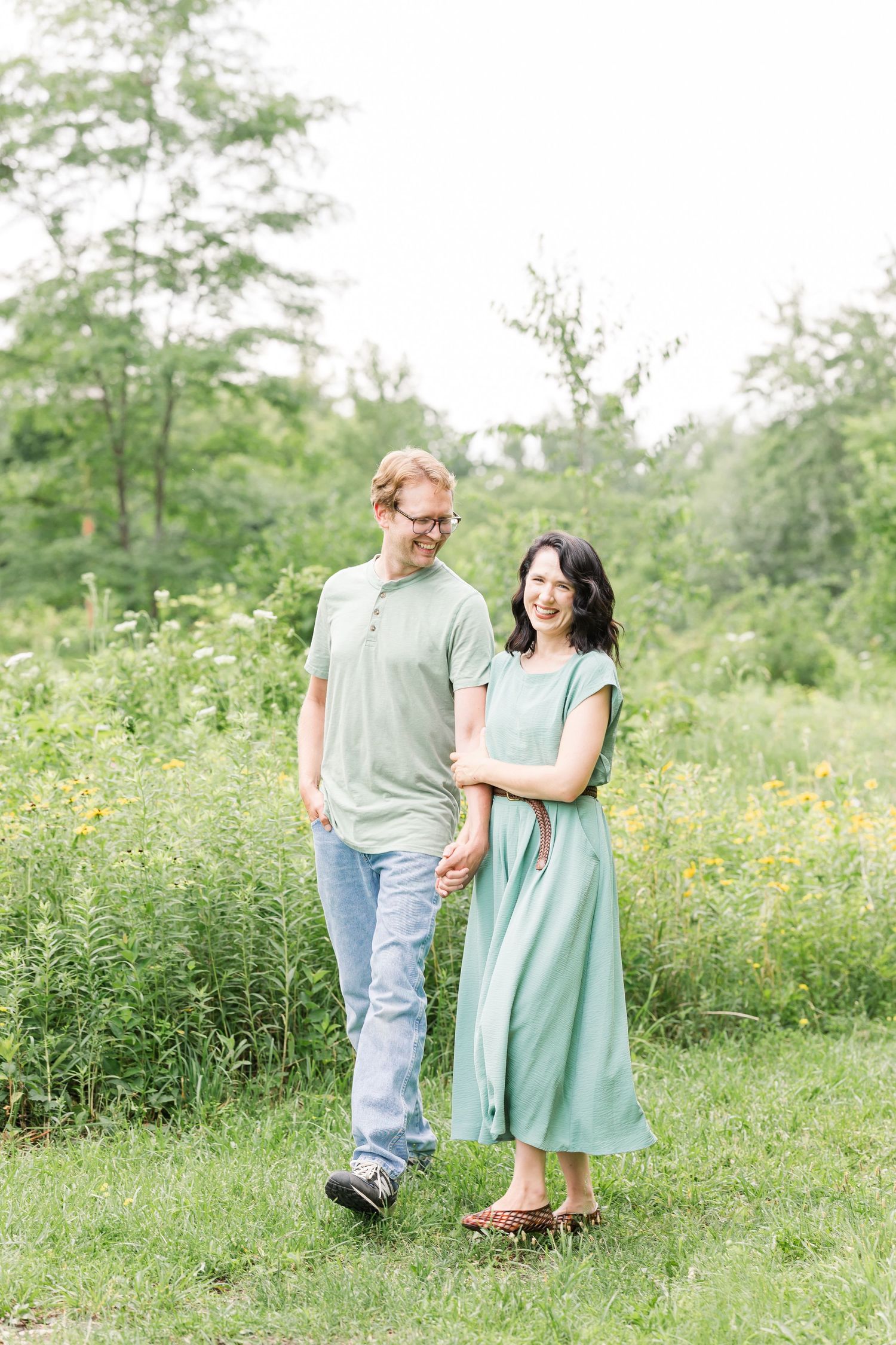 Happy young couple holding hands and walking together in a green meadow with wildflowers.