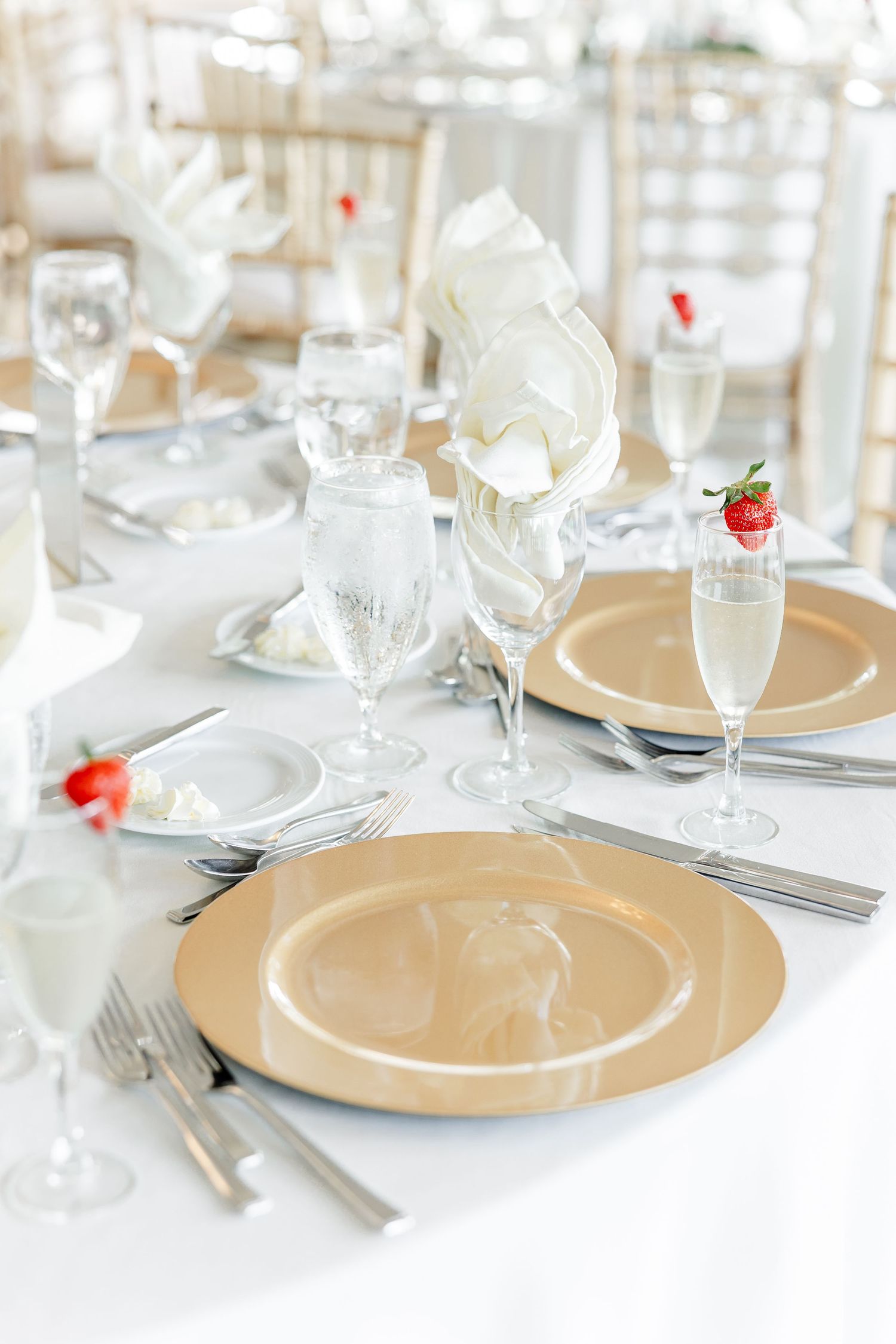 Elegant wedding reception table set with gold charger plates, crystal glasses, and white napkins.