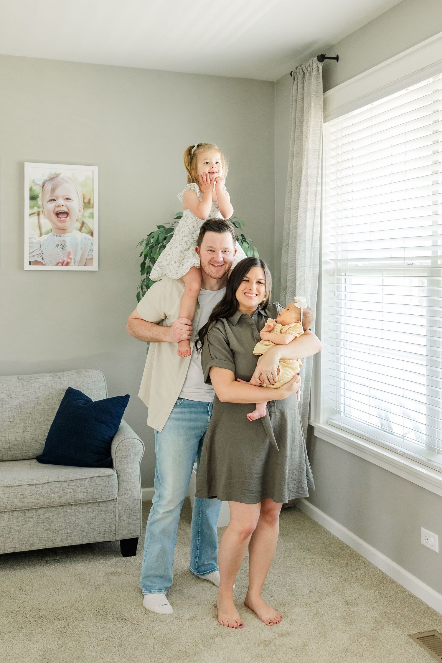 Joyful in-home newborn session with dad holding big sister on his shoulders and mom holding baby girl