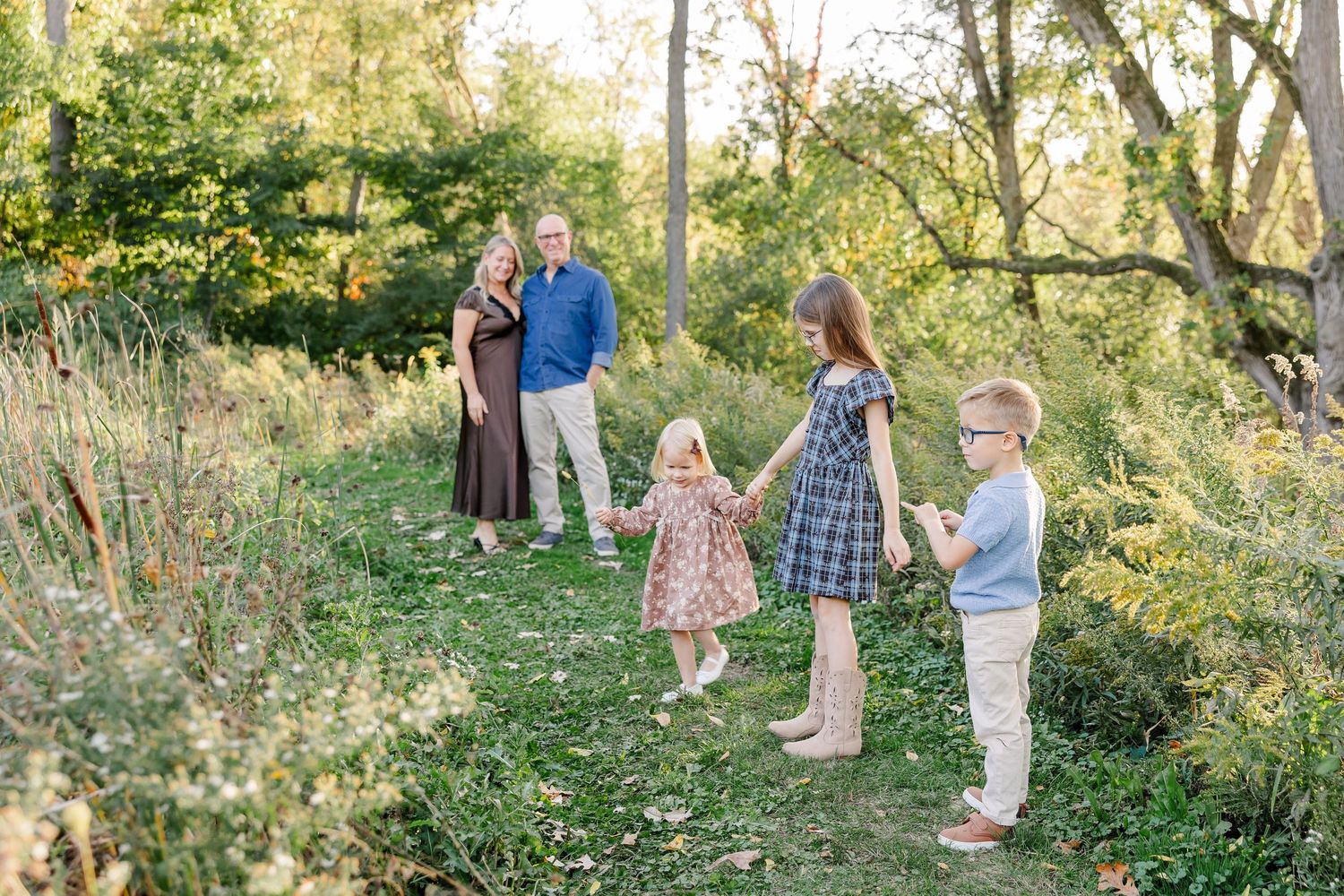 Three children playing together with their parents nearby during backyard family photos in St. Charles, IL.