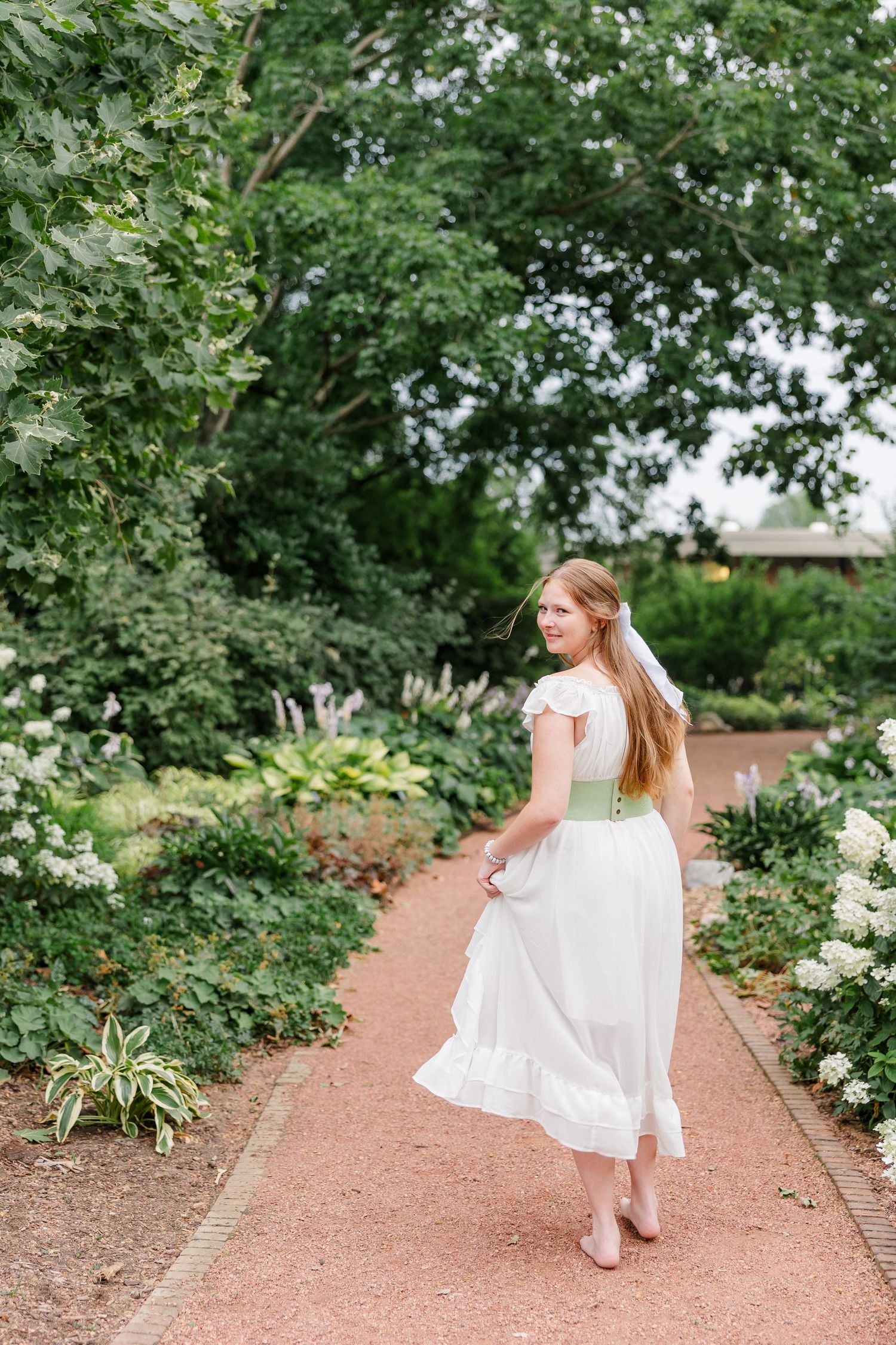 Samantha twirls along a garden path in a flowing white dress during her Cantigny Park senior session.