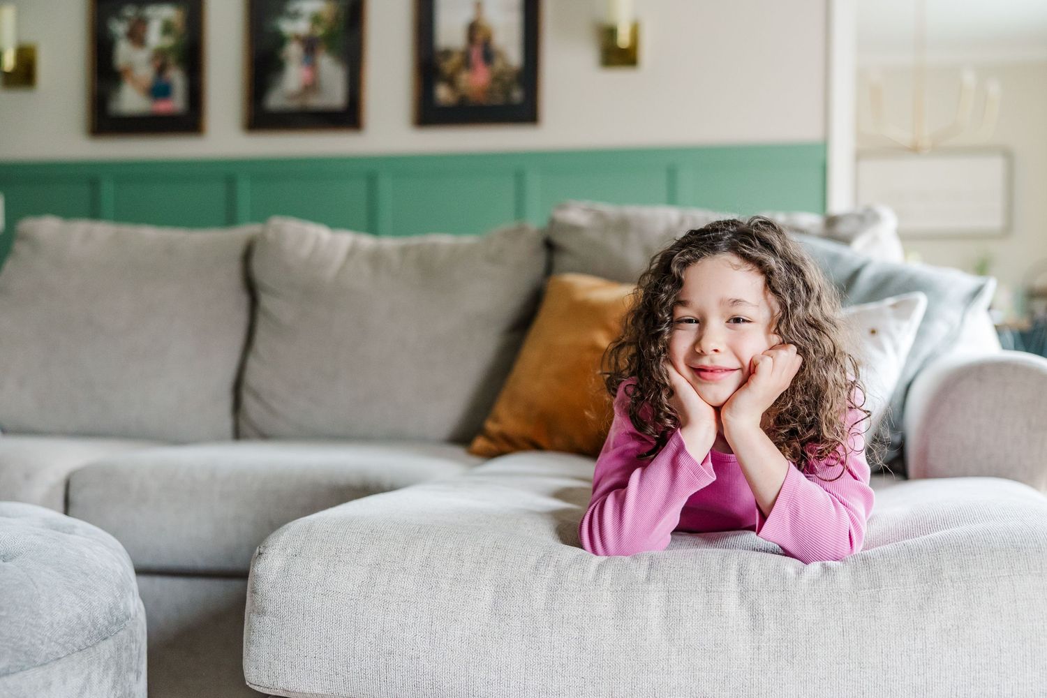 Big sister leaning on ottoman during bright lifestyle newborn session in Crystal Lake, Illinois