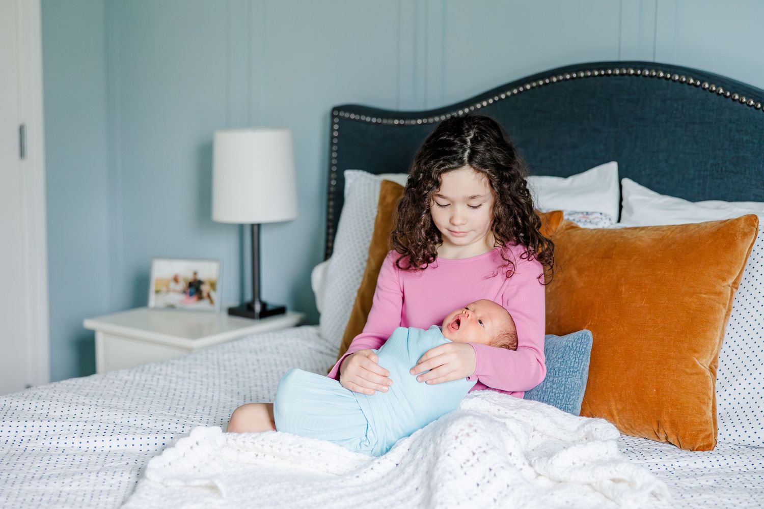 Big sister holding newborn brother on bed during lifestyle newborn session in Crystal Lake, Illinois
